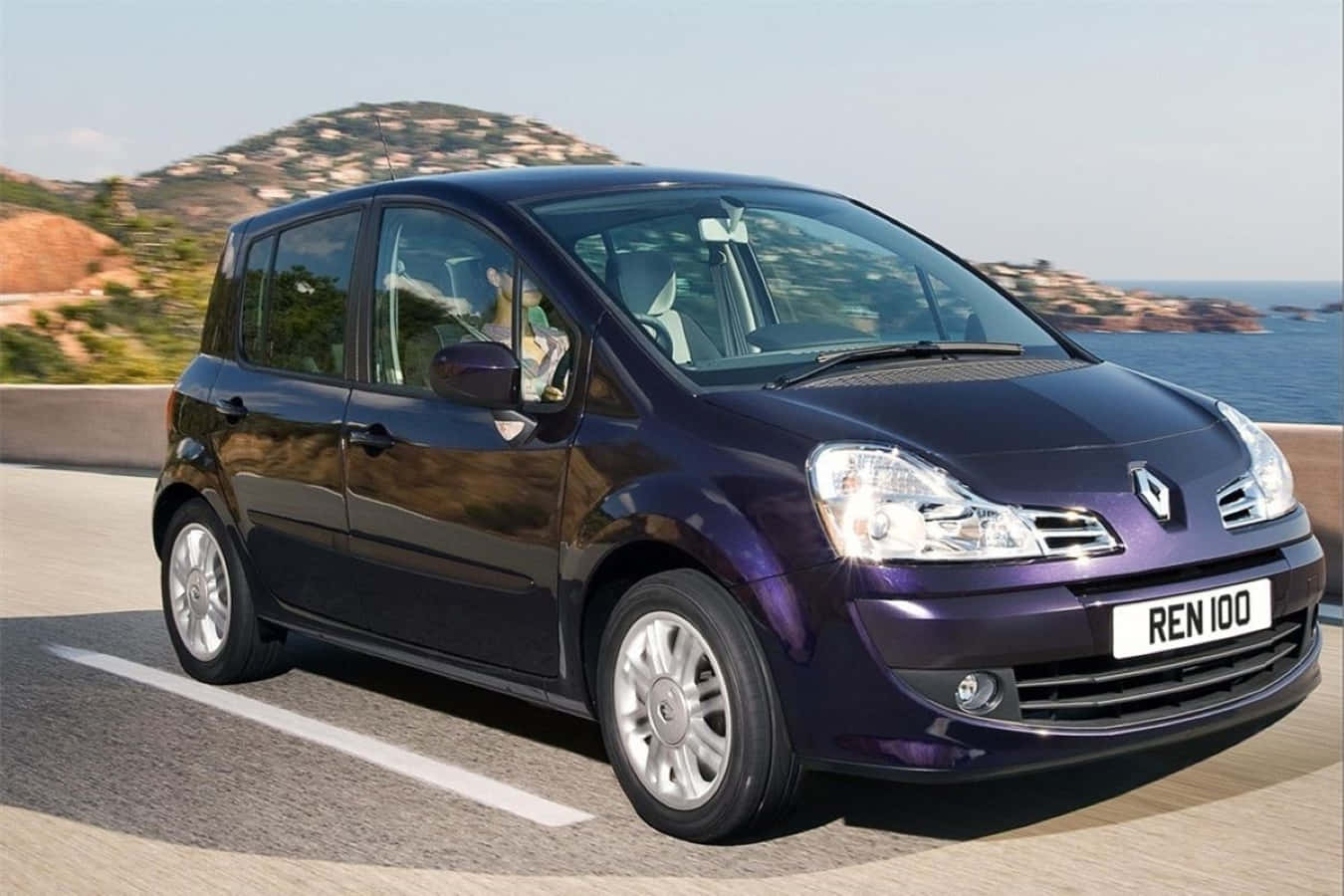 Renault Modus 桌布 壁紙 — 一輛光澤的紫色雷諾100沿著海岸道路行駛，背景有山丘和藍色海洋。