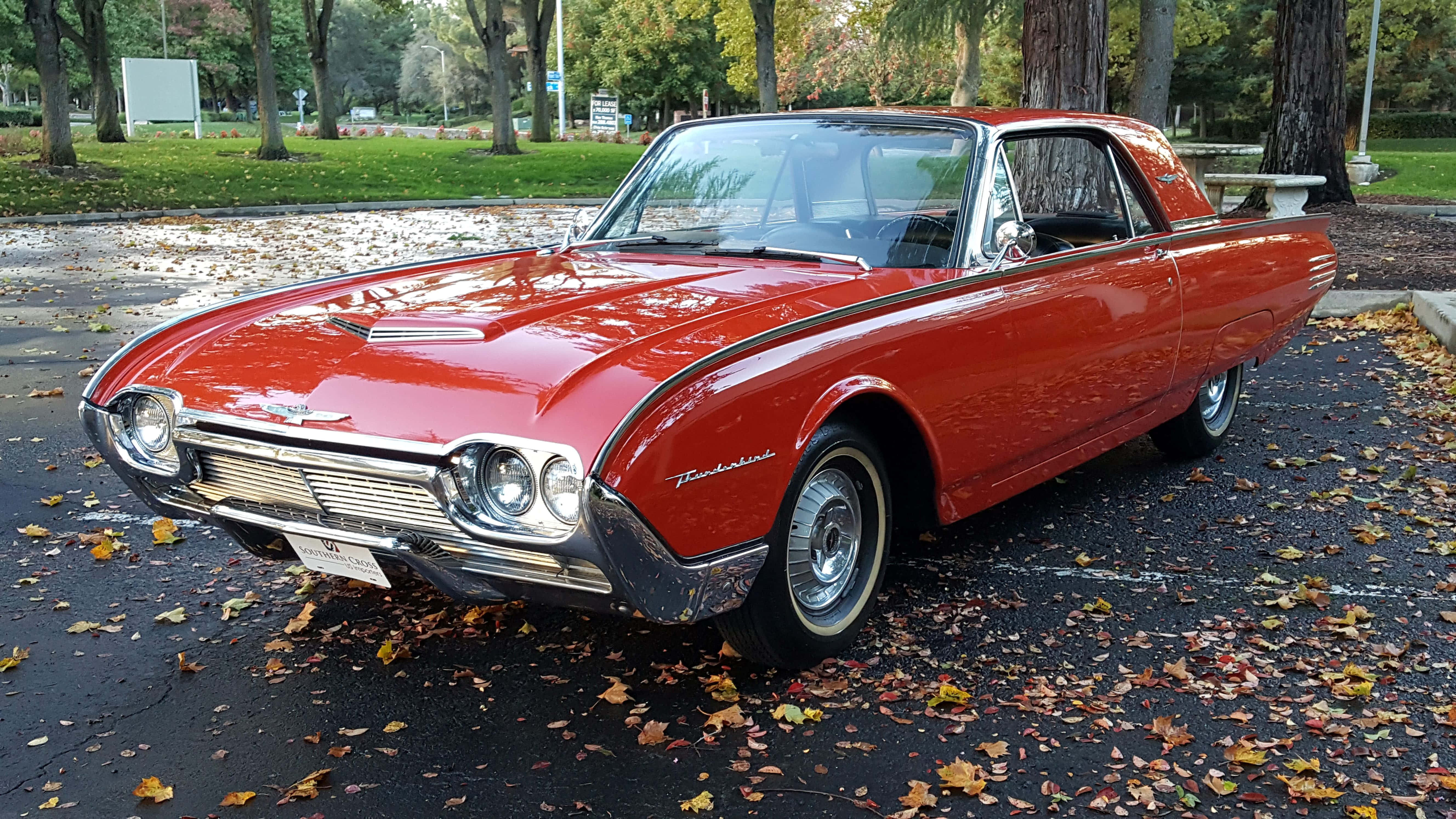 Ford Thunderbird 桌布 壁紙 — 一架閃亮的紅色1960年代福特雷鳥經典汽車停泊在濕漉漉的瀝青停車場上，散落著秋天的落葉。