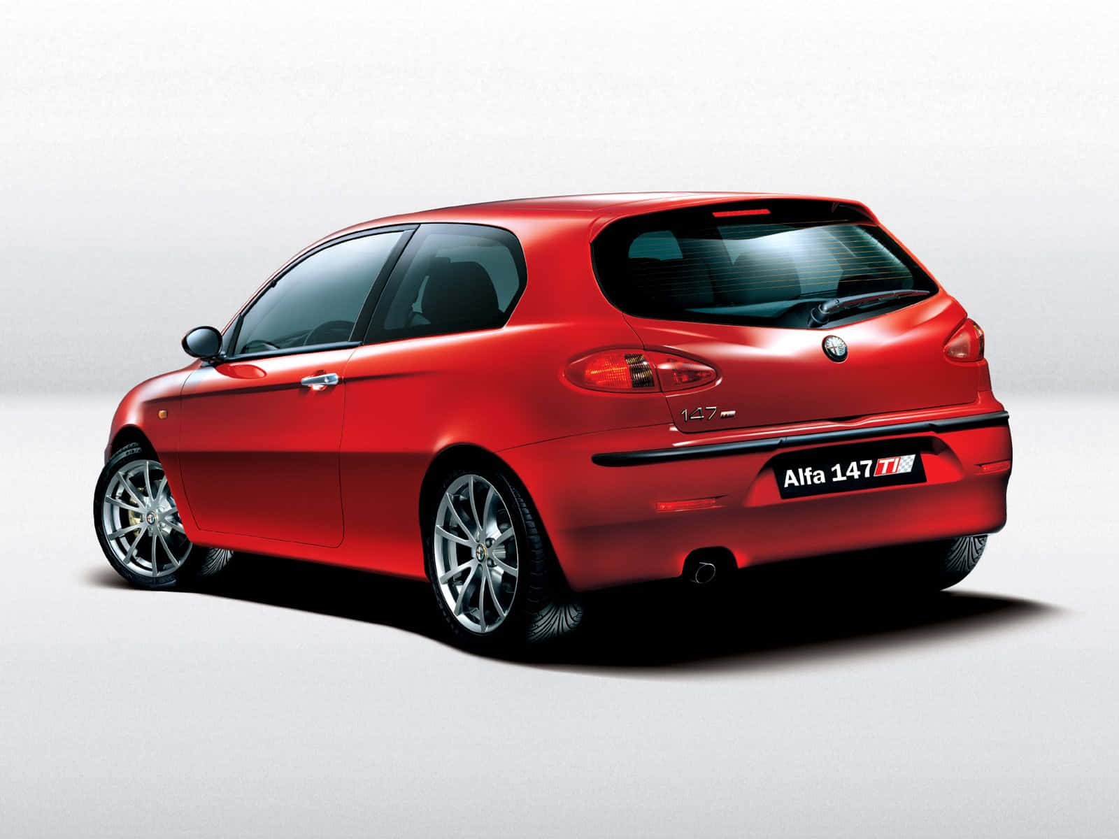 Alfa Romeo 147 桌布 壁紙 — 一輛光澤的紅色Alfa 147 Ti跑車以四分之三後視圖展示在純白色攝影棚背景前。