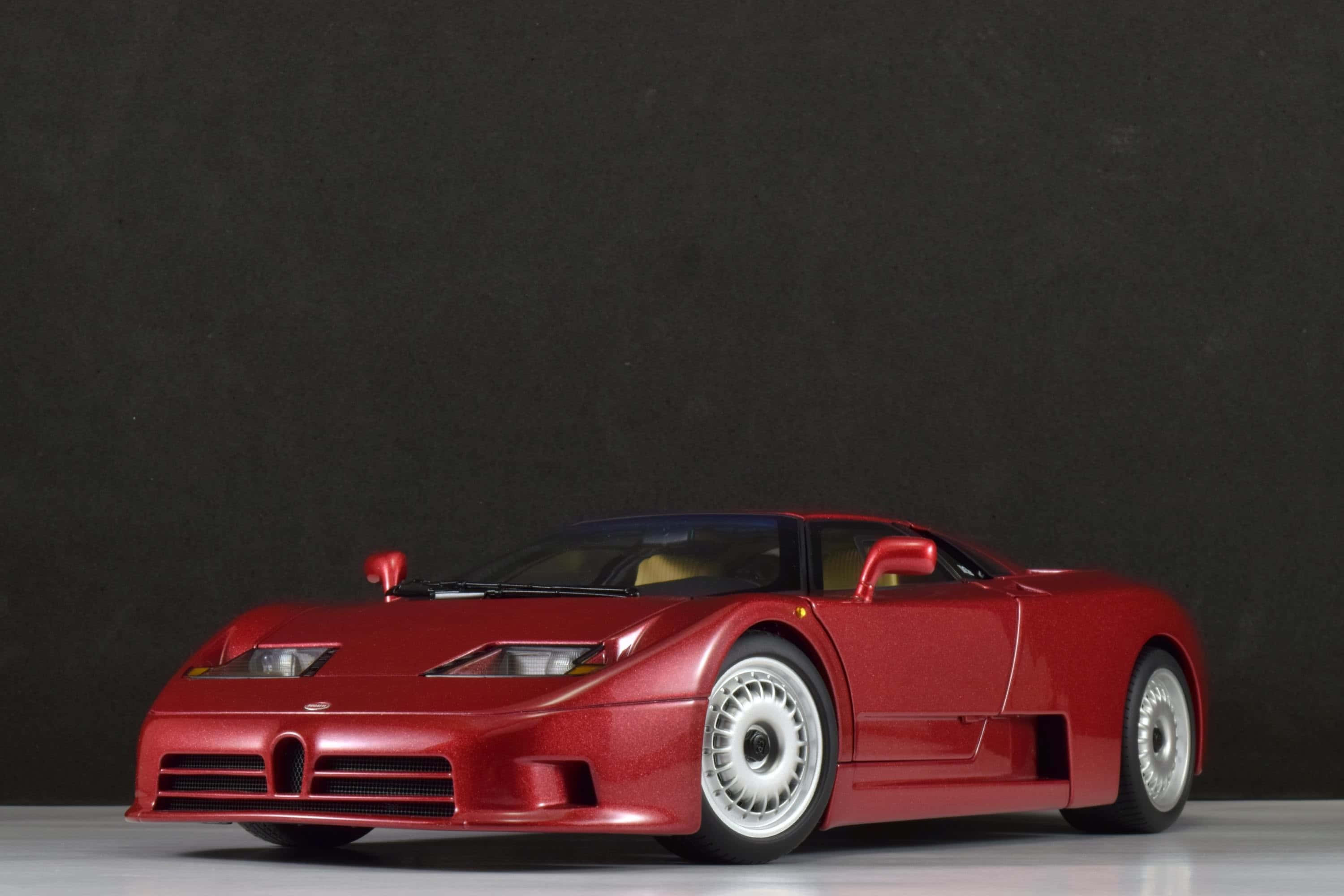 Bugatti Eb110 桌布 壁紙 — 一輛亮紅色Bugatti EB110超級跑車模型，放在深灰色工作室背景前，配有白色車輪。