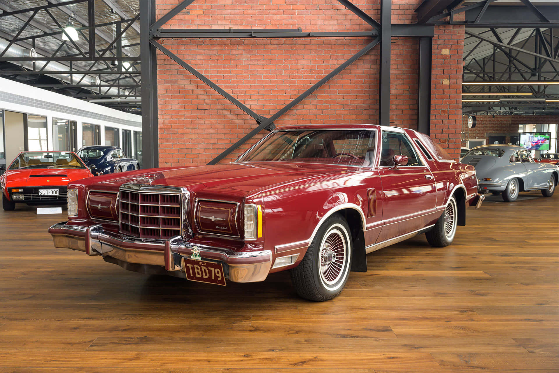 Ford Thunderbird 桌布 壁紙 — 一輛光澤的紅色經典肌肉車，帶有鍍鉻細節，醒目地放置在一個寬敞的磚牆和硬木地板的汽車博物館中。