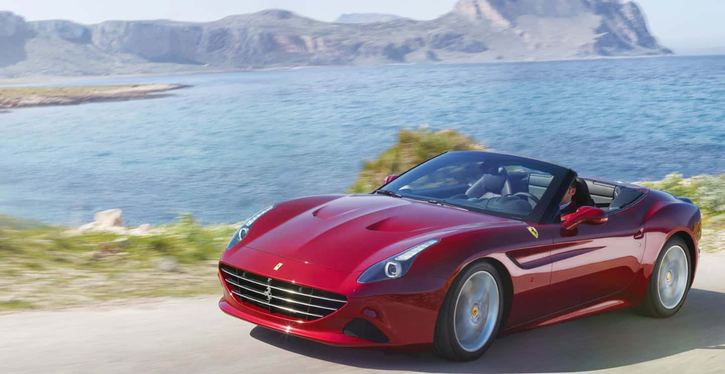 Ferrari California T 桌布 壁紙 — 一輛亮紅色法拉利 California 敞篷車沿著海岸公路飛馳，背景是碧綠的海水和岩石峭壁。
