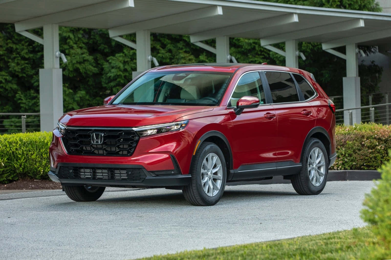 Honda Cr-v 桌布 壁紙 — 一輛亮紅色本田SUV停放在現代車棚下，背景有綠色灌木和樹木。
