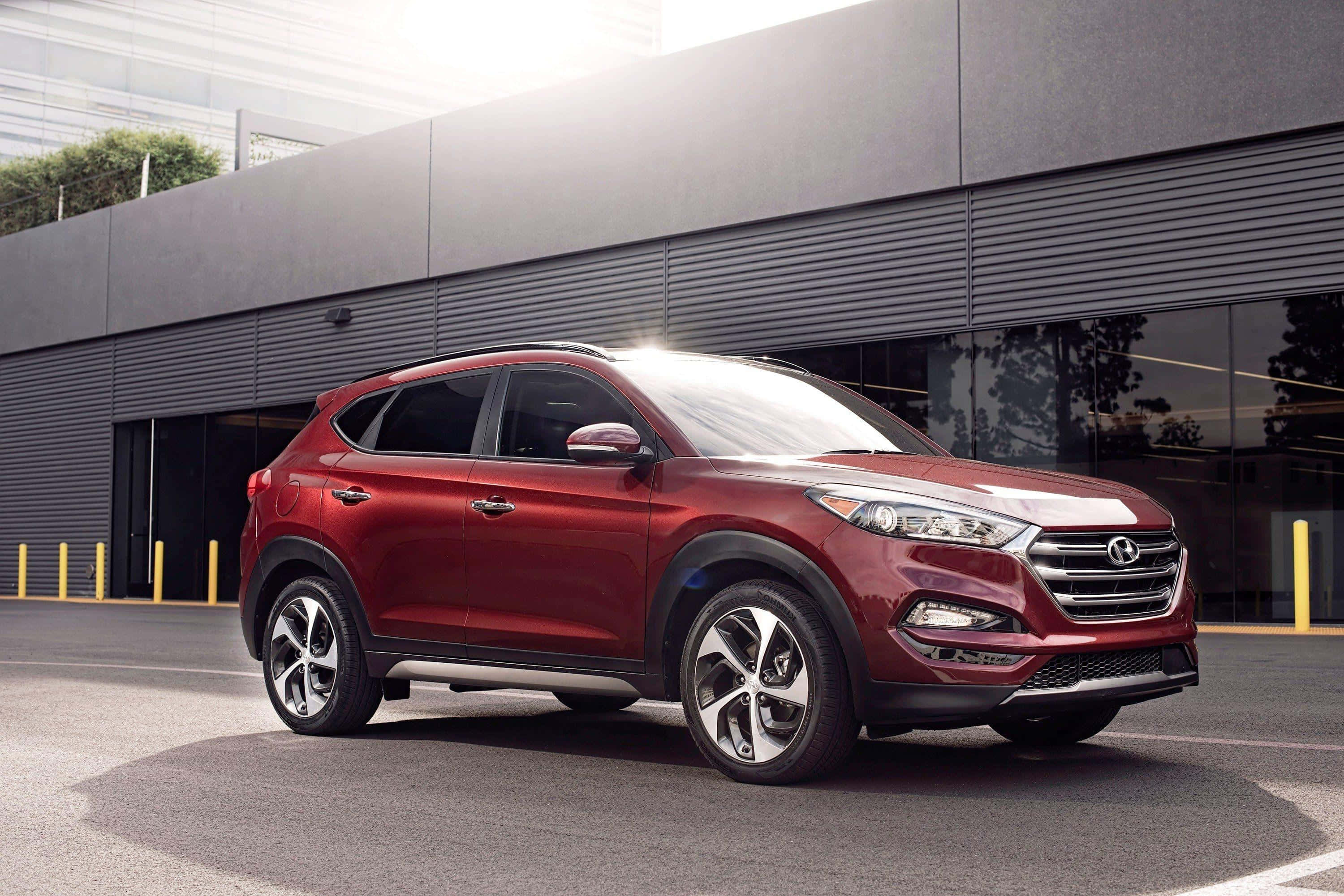 Hyundai Tucson 桌布 壁紙 — 一輛光澤紅色Hyundai Tucson SUV停在一棟帶有反光窗戶的現代灰色建築前。