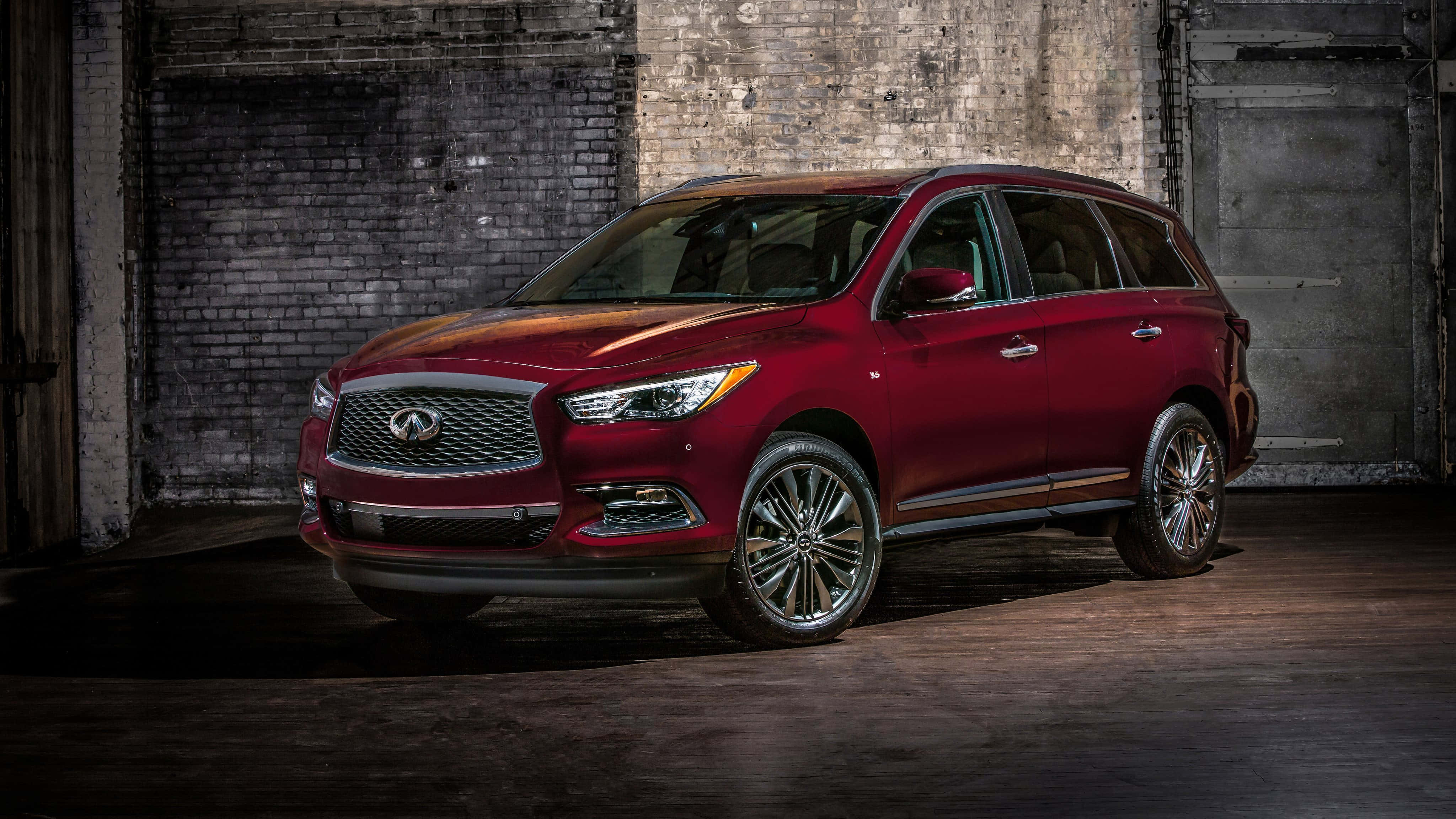 Infiniti Qx60 桌布 壁紙 — 一輛光澤的紅色 Infiniti QX60 SUV 在一個粗糙的工業倉庫中，以裸露的磚牆為背景，被戲劇性地照亮。