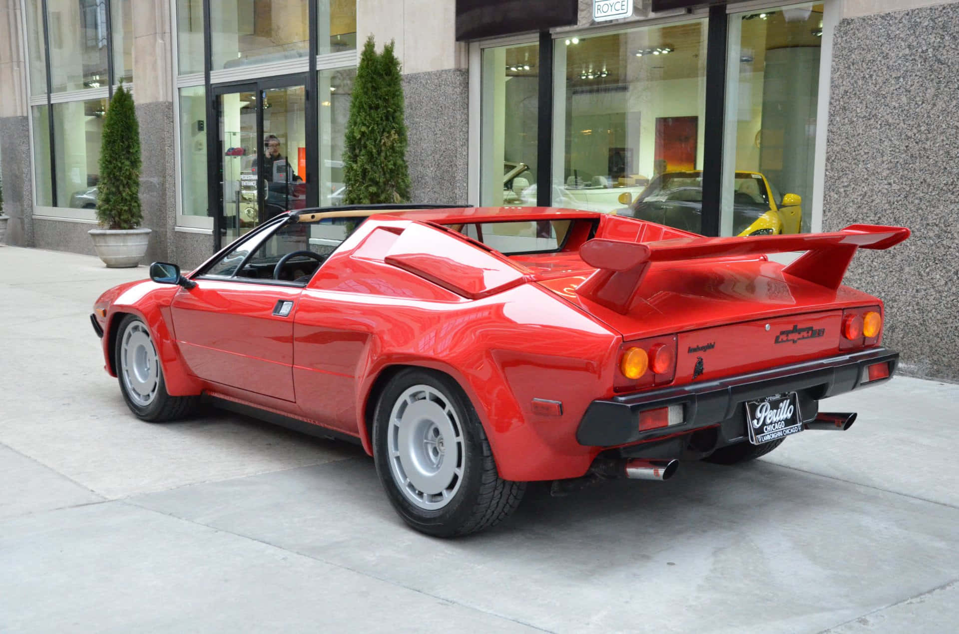 Lamborghini Jalpa 桌布 壁紙 — 一架亮紅色林寶堅尼Countach LP400S跑車停泊在玻璃幕牆建築物前的城市行人路上。