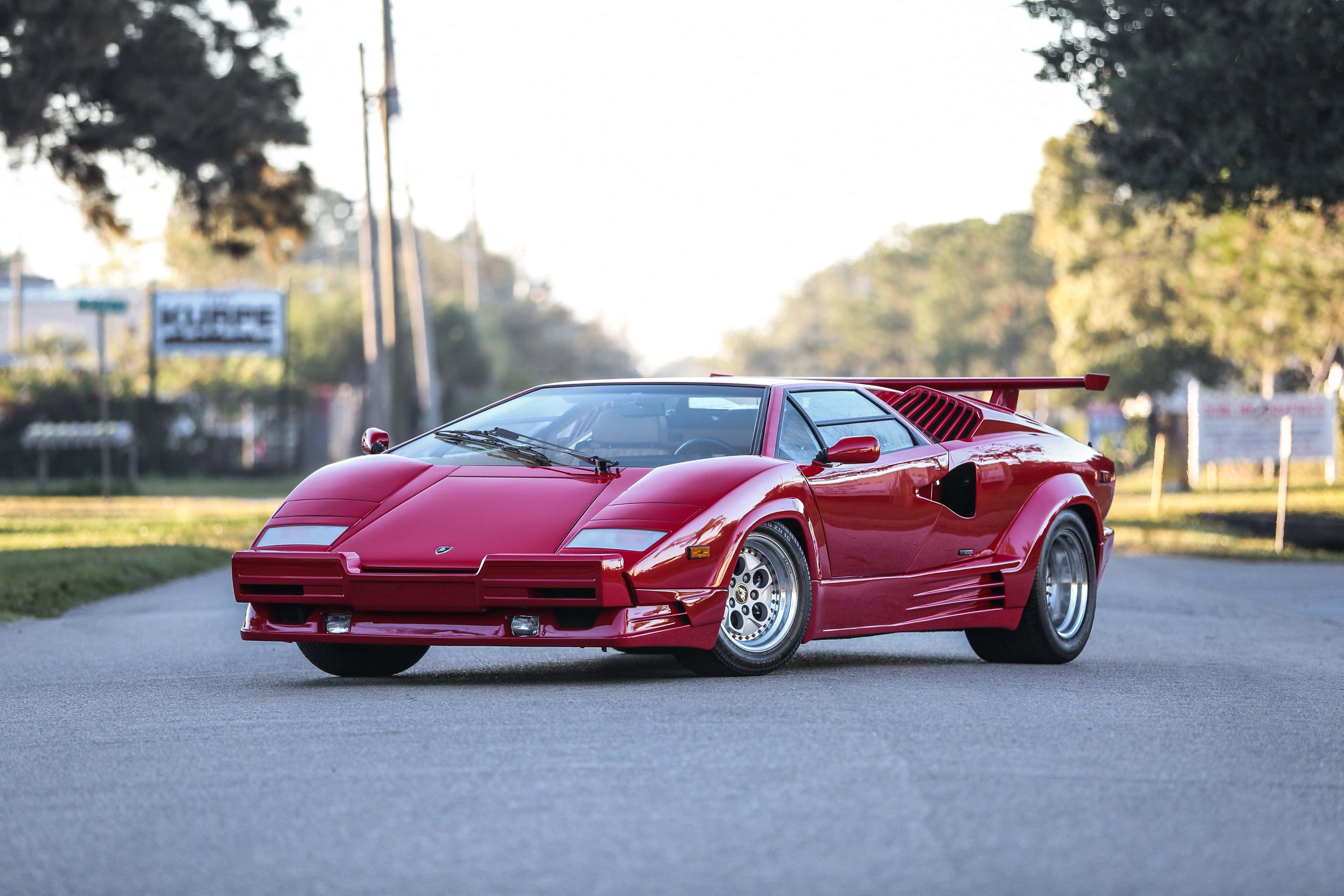 Lamborghini Countach 桌布 壁紙 — 一輛亮紅色林寶堅尼Countach在黃金夕陽光輝沐浴下的林蔭大道上飛馳。
