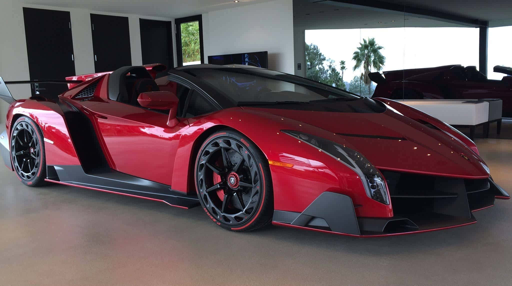 Lamborghini Veneno 桌布 壁紙 — 一輛光澤的紅色林寶堅尼 Veneno 開篷跑車在明亮的室內燈光下，在一個時尚的現代車庫中閃閃發光，外面可以看到棕櫚樹。
