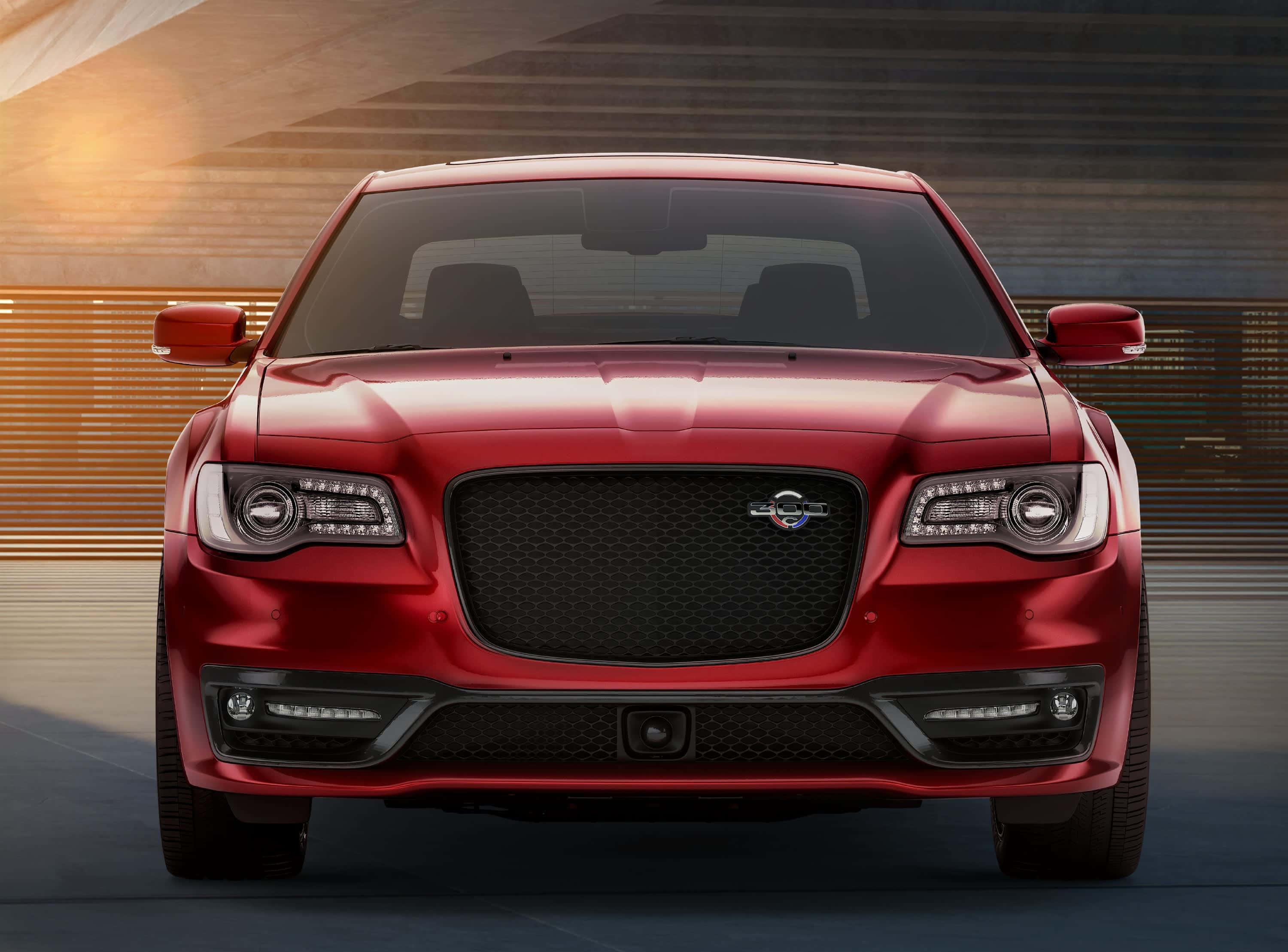 Chrysler 300 桌布 壁紙 — 一輛光澤的紅色豪華轎車在溫暖的金色燈光下正面朝向現代建築背景。