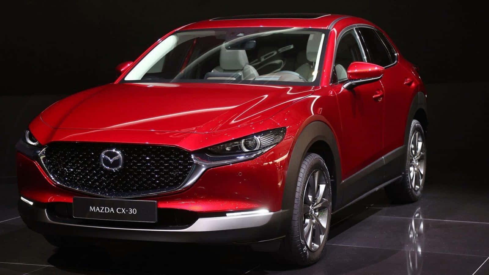 Mazda Cx-30 桌布 壁紙 — 一輛光澤的紅色Mazda CX-30 SUV在工作室燈光下展示在深色反光舞台上。