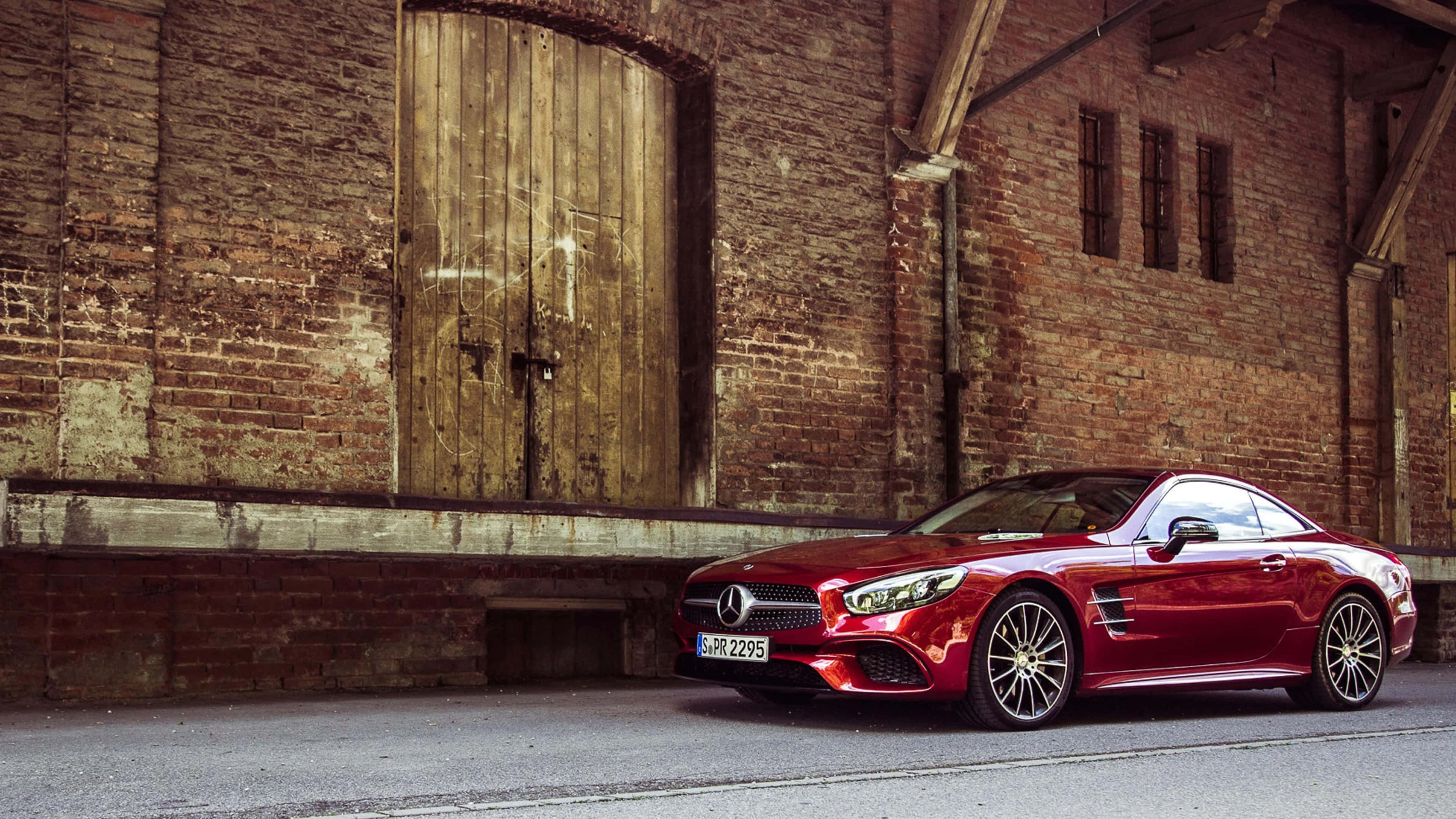 Mercedes Benz Sl-class 桌布 壁紙 — 一架亮紅色平治AMG SL63跑車停泊在一個帶有大型木門、風化了的磚倉庫前。