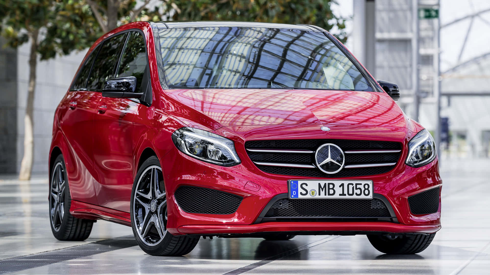 Mercedes Benz B-class 桌布 壁紙 — 一輛亮紅色的梅賽德斯-奔馳B級車停在鋪磚的城市廣場上，玻璃建築反射在引擎蓋上。