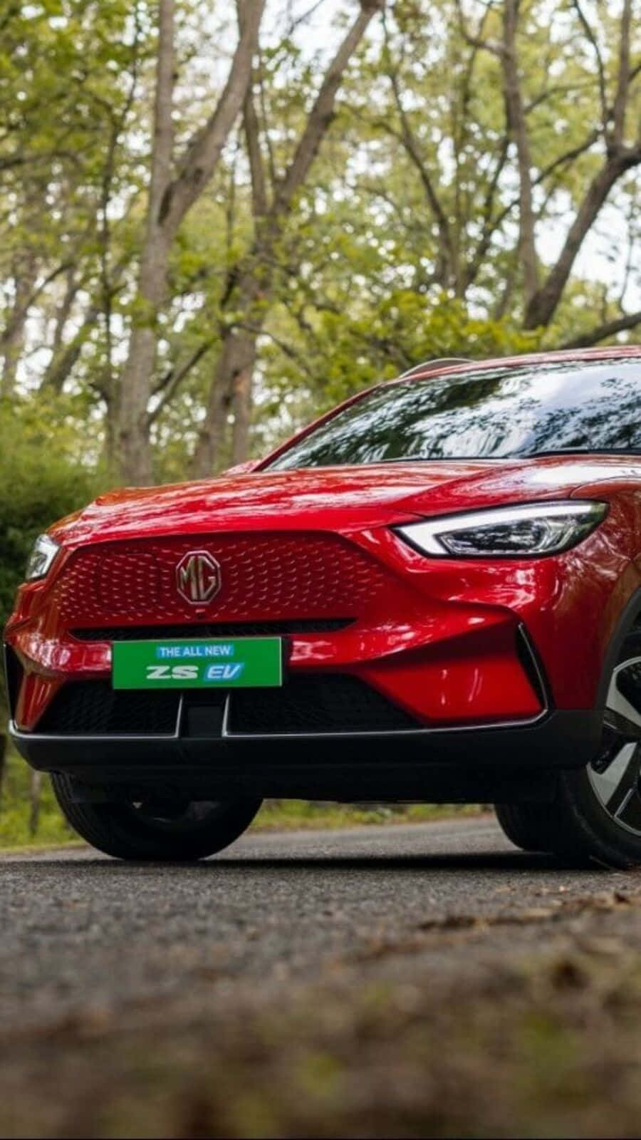  壁紙 — 一輛亮紅色MG ZS EV電動SUV停泊在森林道路上，背景樹木呈現柔和焦點。
