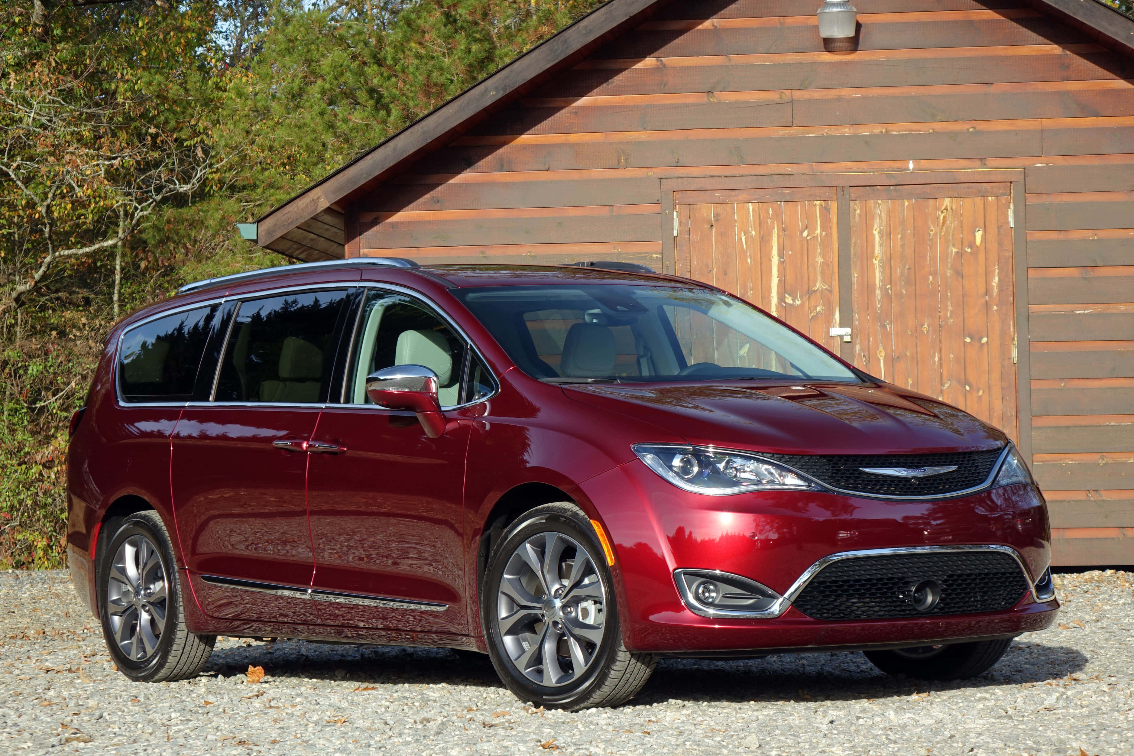 Chrysler Pacifica 桌布 壁紙 — 一輛光亮的紅色小型貨車停在碎石路上，前面是木屋，背景有秋天的樹木。