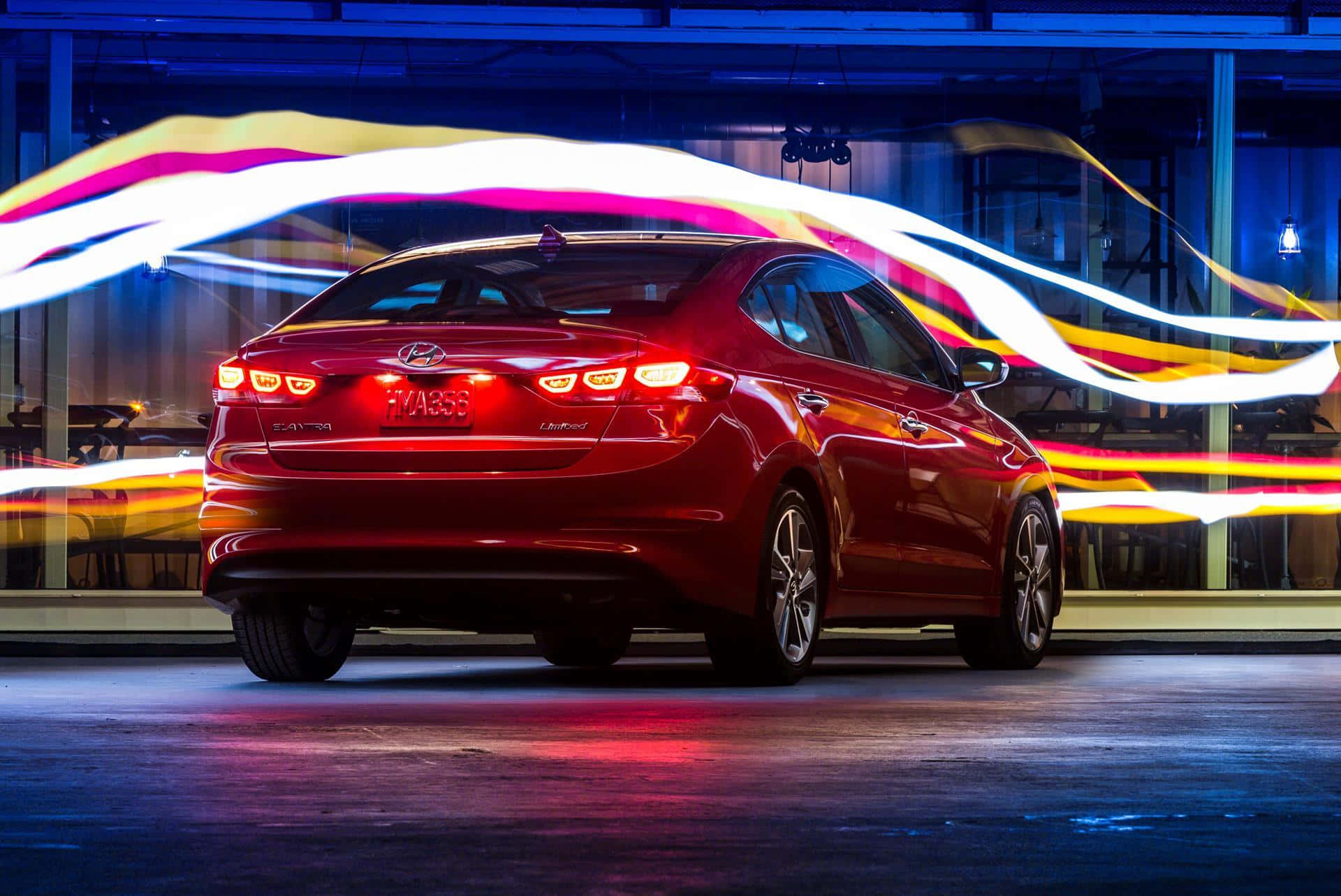 Hyundai Elantra 桌布 壁紙 — 一輛光澤的紅色轎車停放在室內，在藍色環境燈光下，有鮮豔的光條圍繞它旋轉。