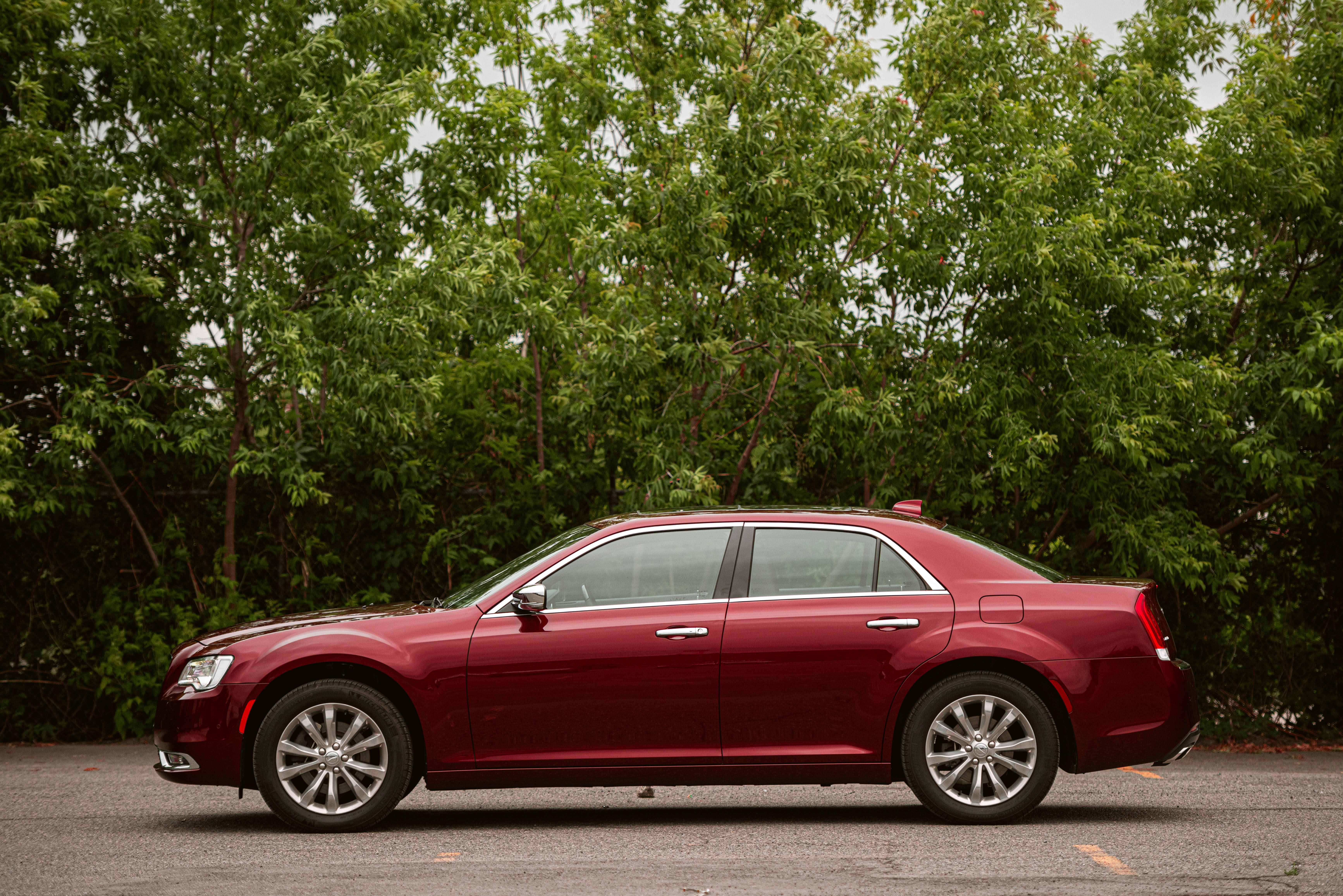 Chrysler 300 桌布 壁紙 — 一輛光澤的紅色轎車停在瀝青路上，背後有茂密的綠樹，天空多雲。