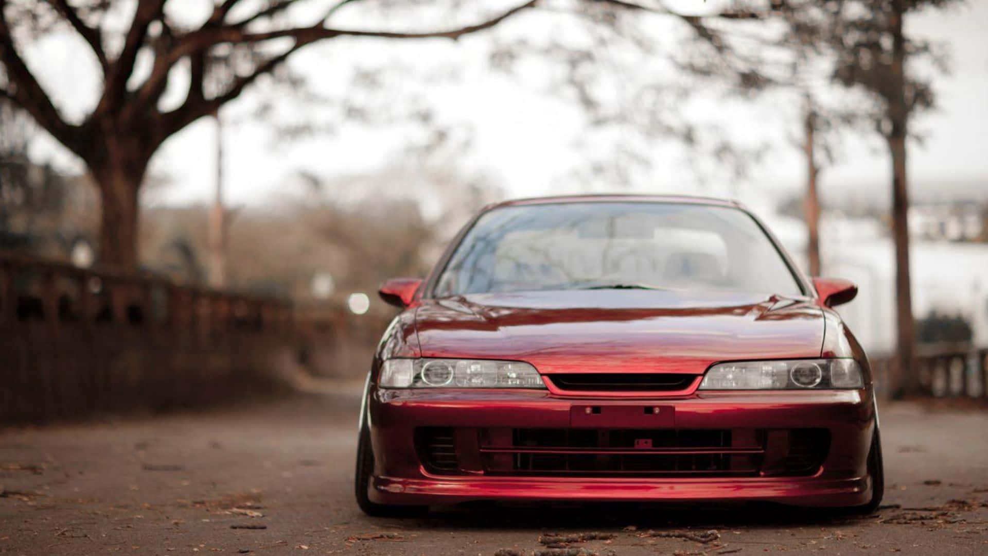 Acura Integra 桌布 壁紙 — 一架亮紅色跑車配備定制前保險槓，低趴在一條林蔭大道上，處於柔和陰天光線下。