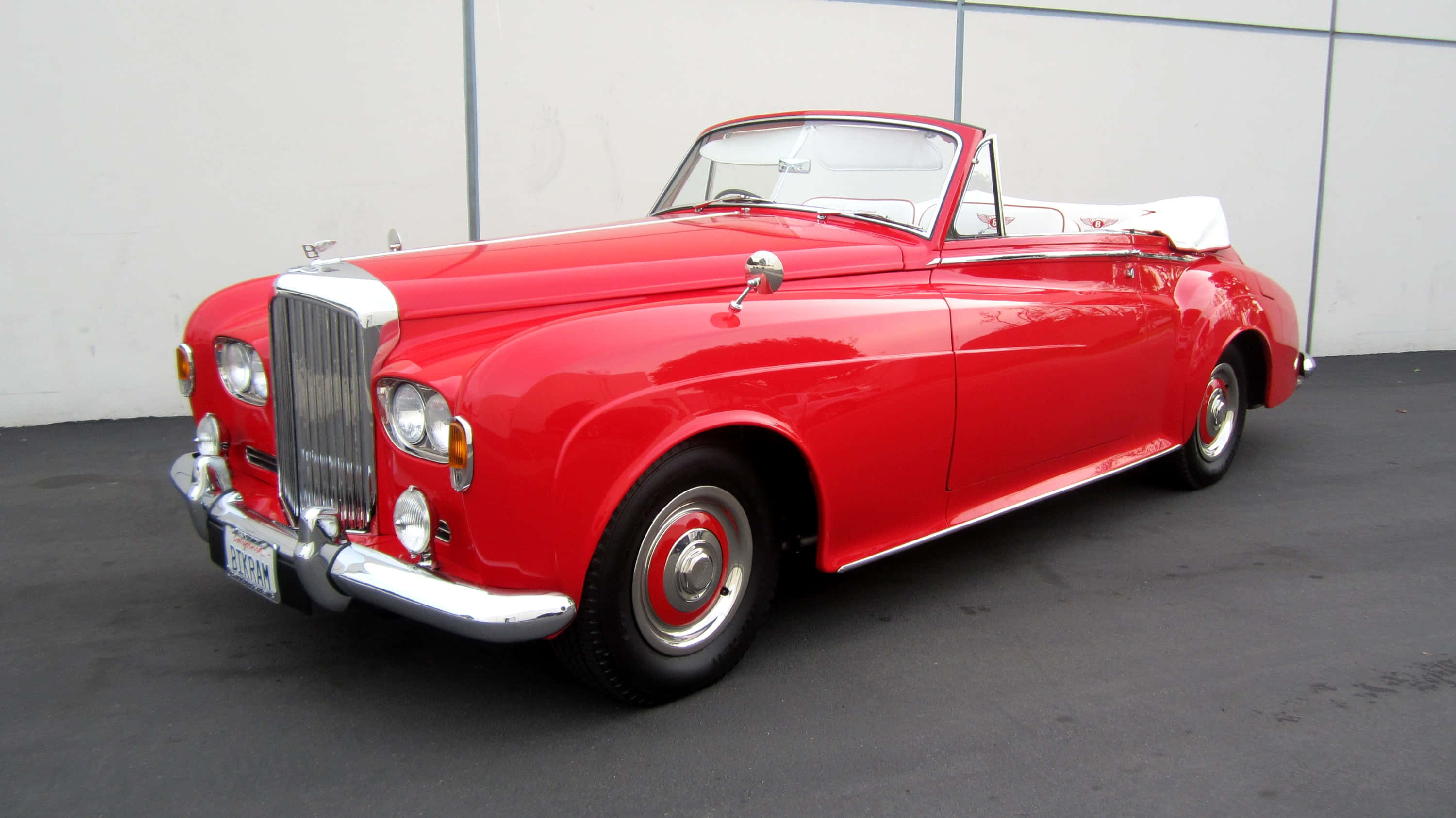Bentley S3 桌布 壁紙 — 一輛光澤的紅色復古敞篷跑車，配備白色內飾和鍍鉻裝飾，停放在純白色牆壁前。