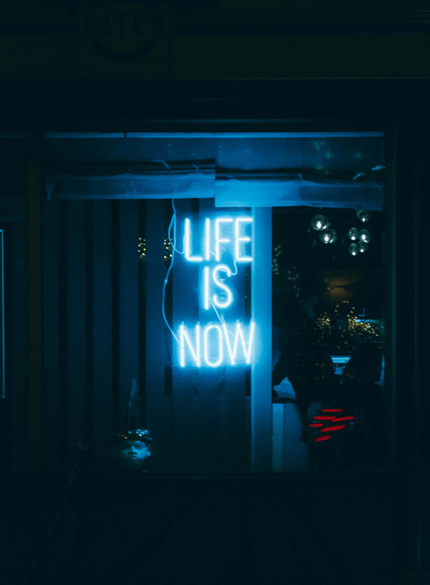  壁紙 — 一個發光的藍色霓虹燈牌，上面寫著「LIFE IS NOW」，在夜晚照亮了漆黑的商店櫥窗。