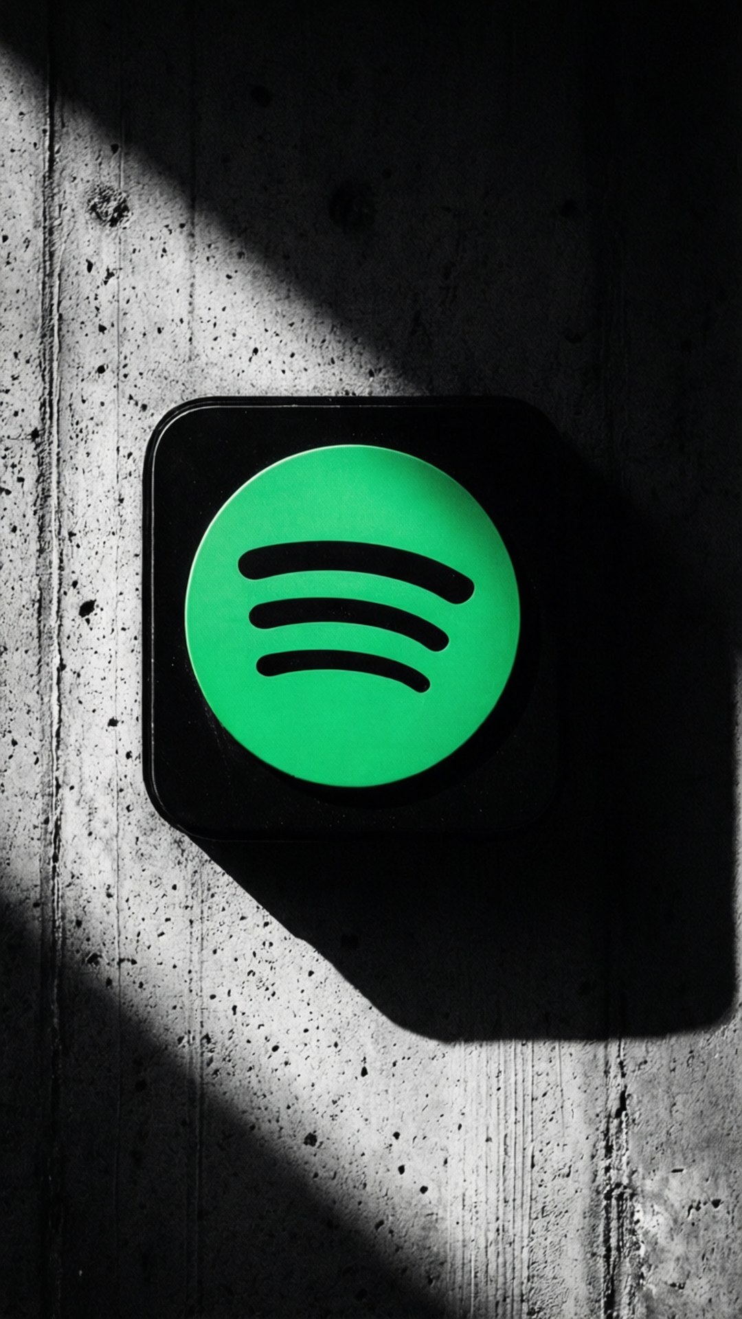 桌布 壁紙 — 一個發光的綠色Spotify標誌，位於黑色正方形上，安裝在帶有紋理的混凝土牆上，帶有戲劇性的對角線陰影。