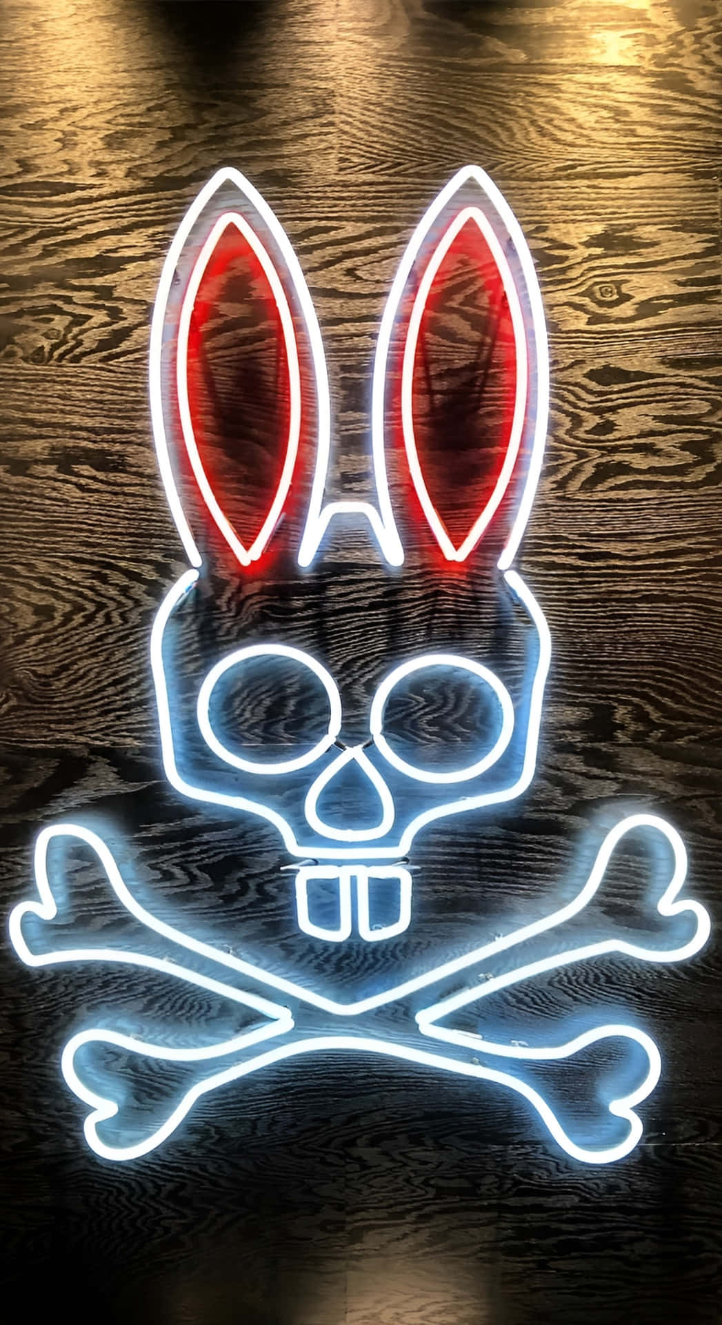  壁紙 — 一個發光的霓虹燈牌，在深色木質背景上描繪了一個帶有兔耳朵和交叉骨頭的骷髏頭。