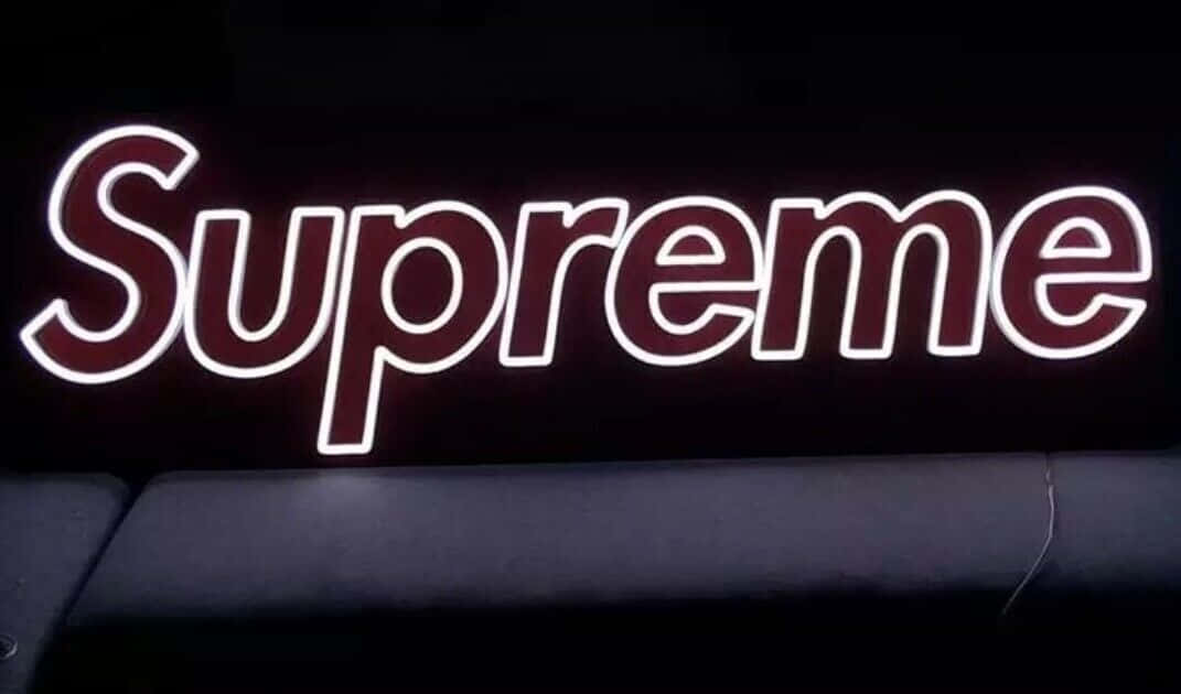 霓虹燈 Supreme 標誌在黑色沙發上方的黑暗牆壁上發光。