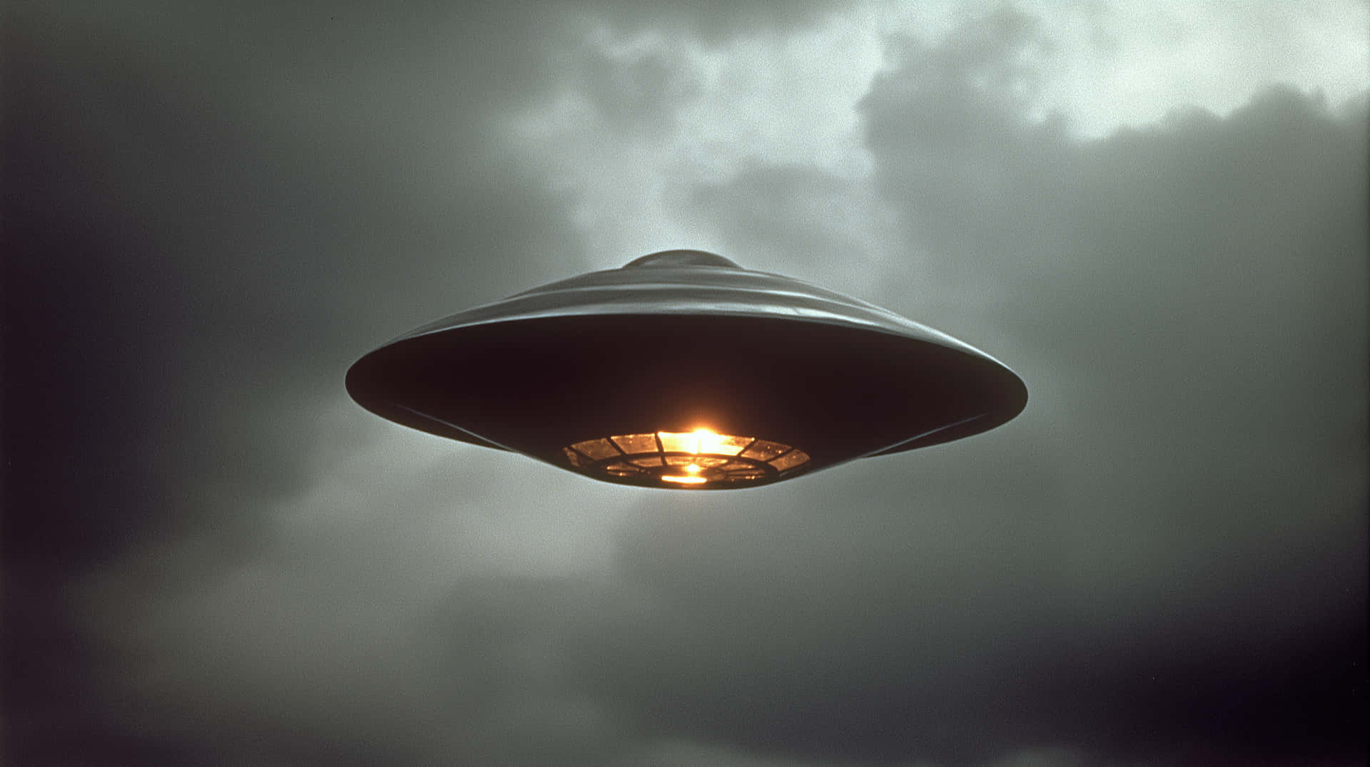 一個中心發光的金屬UFO在風暴般的灰色天空中盤旋。