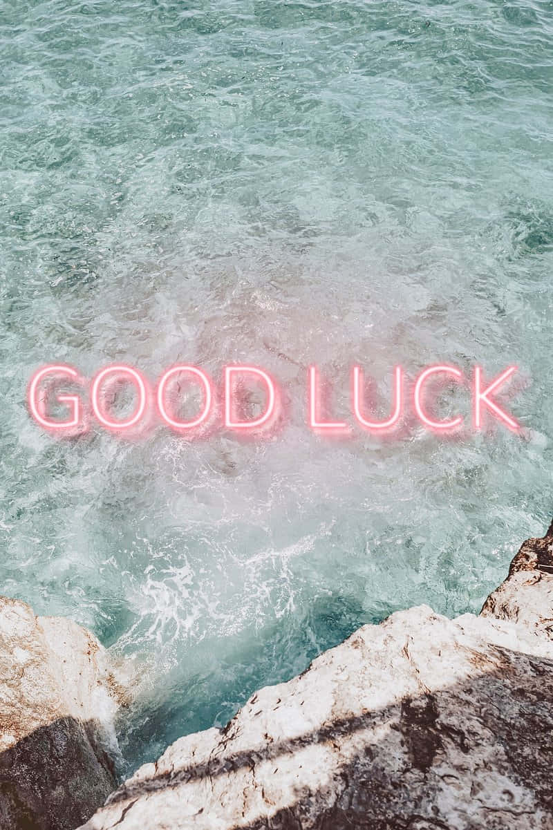  壁紙 — 一個發光的粉紅色霓虹燈牌，上面寫著 good luck，漂浮在碧綠的海浪拍打崎嶇懸崖的上方。