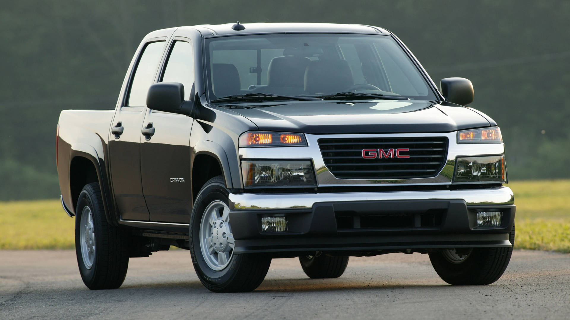 GMC車輛置身廣闊草地 壁紙 — 一輛時尚的黑色GMC Canyon皮卡車停在鋪砌的道路上，背景是草地和樹木。
