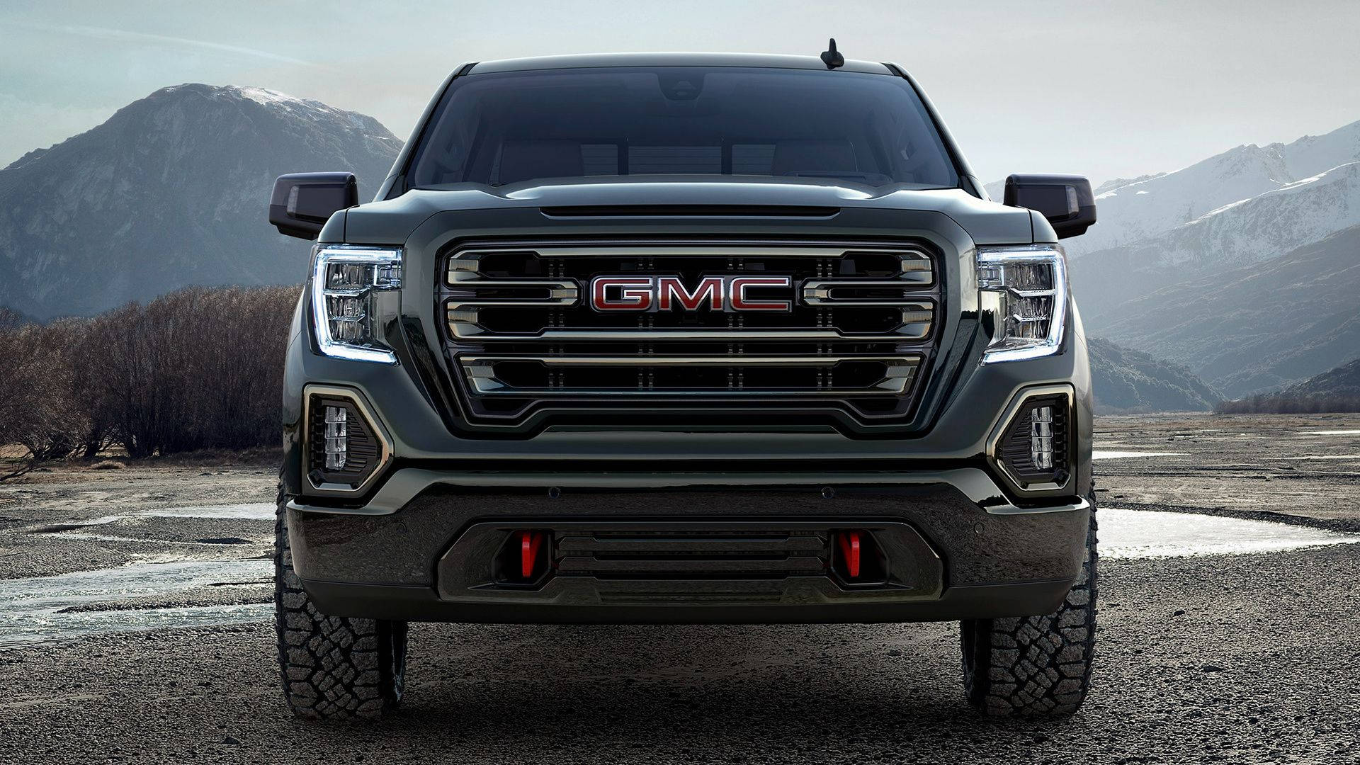 GMC Sierra車輛特寫 壁紙 — 一輛黑色GMC卡車在碎石路上向前行駛，背景是白雪覆蓋的山脈。