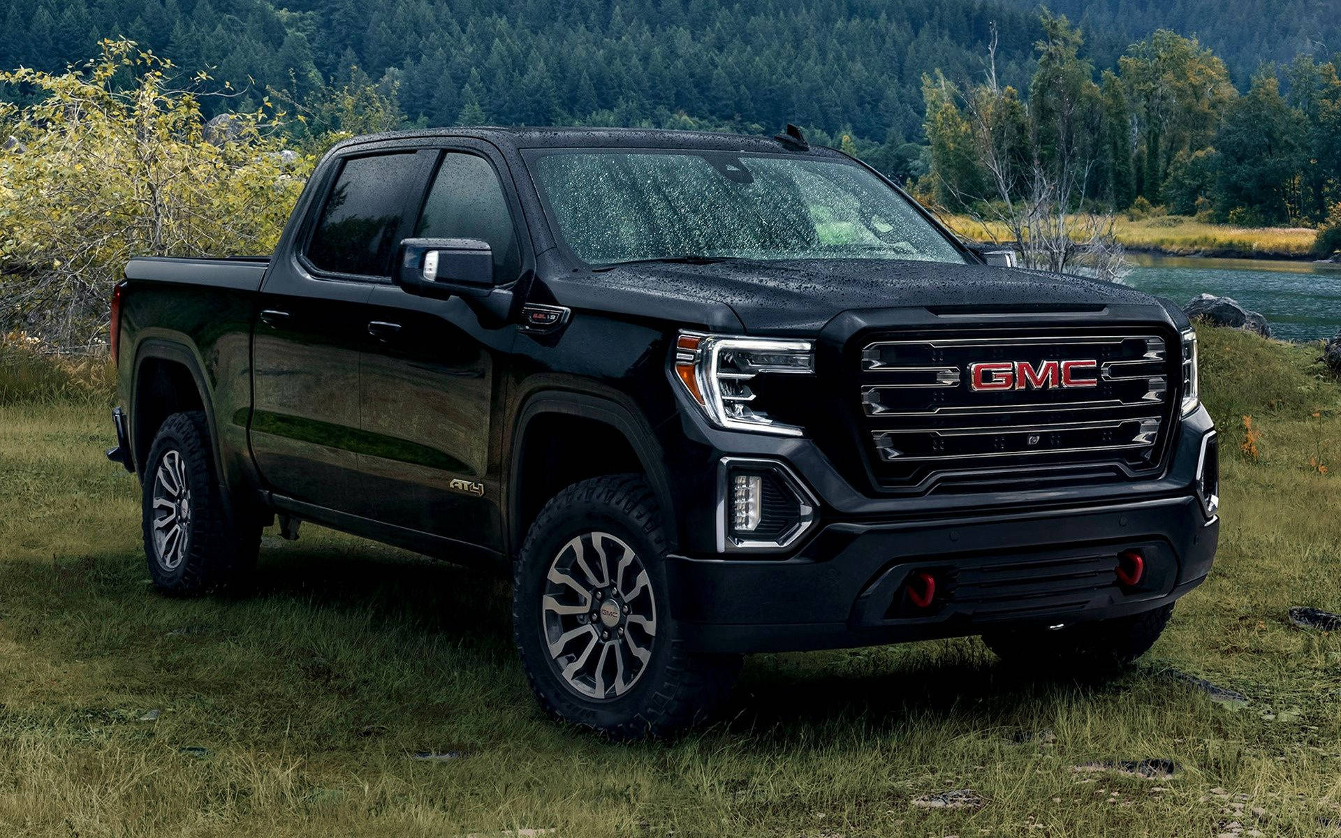 GMC停於草地 壁紙 — 一輛時尚的黑色GMC Sierra AT4 pickup truck在日光下停泊在靠近森林河岸的草地上。