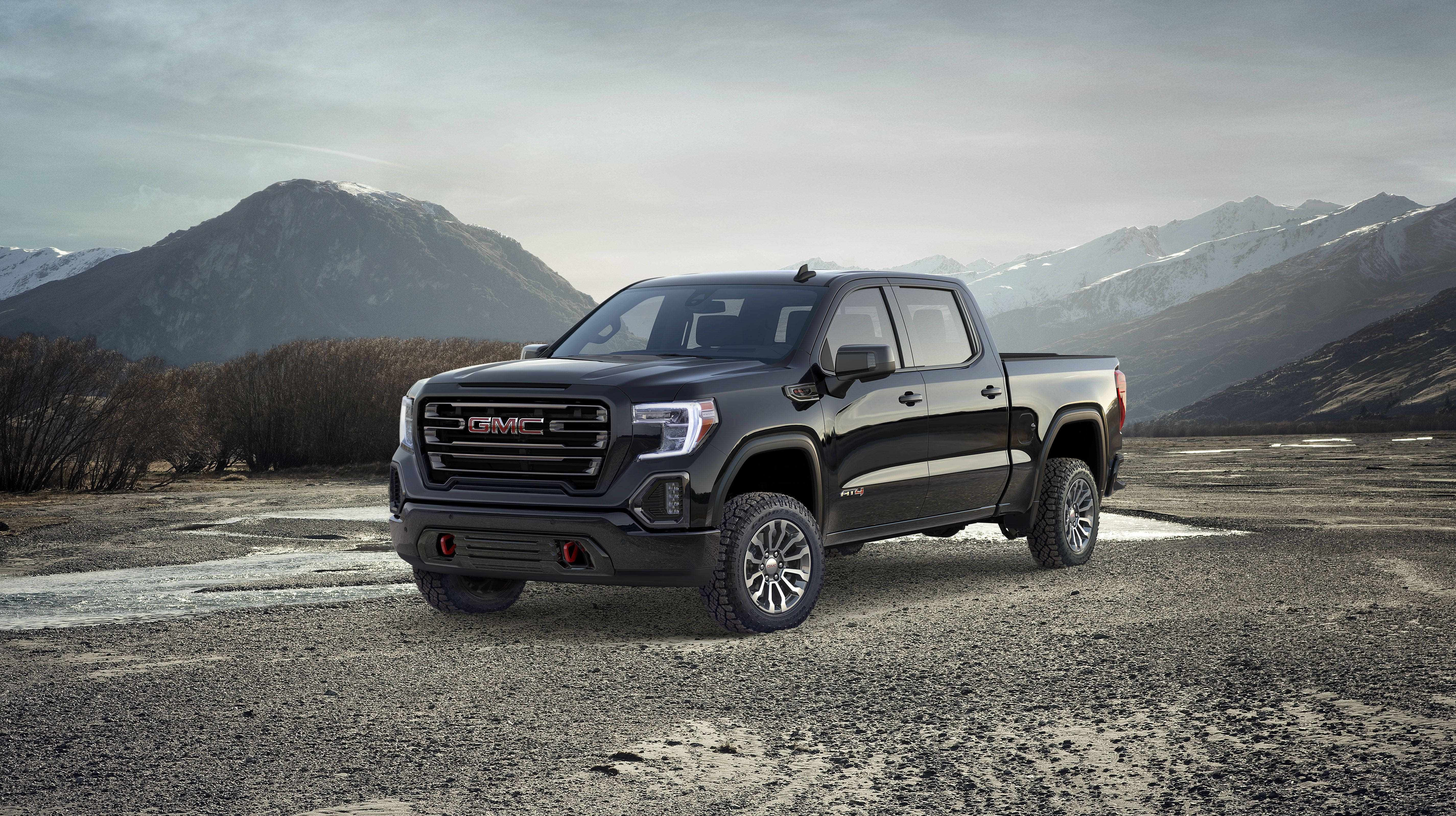 GMC車輛置身霧氣山景 壁紙 — 一架時尚的黑色 GMC Sierra 皮卡車停泊在礫石平原上，背後有積雪的山峰在陰天中聳立。