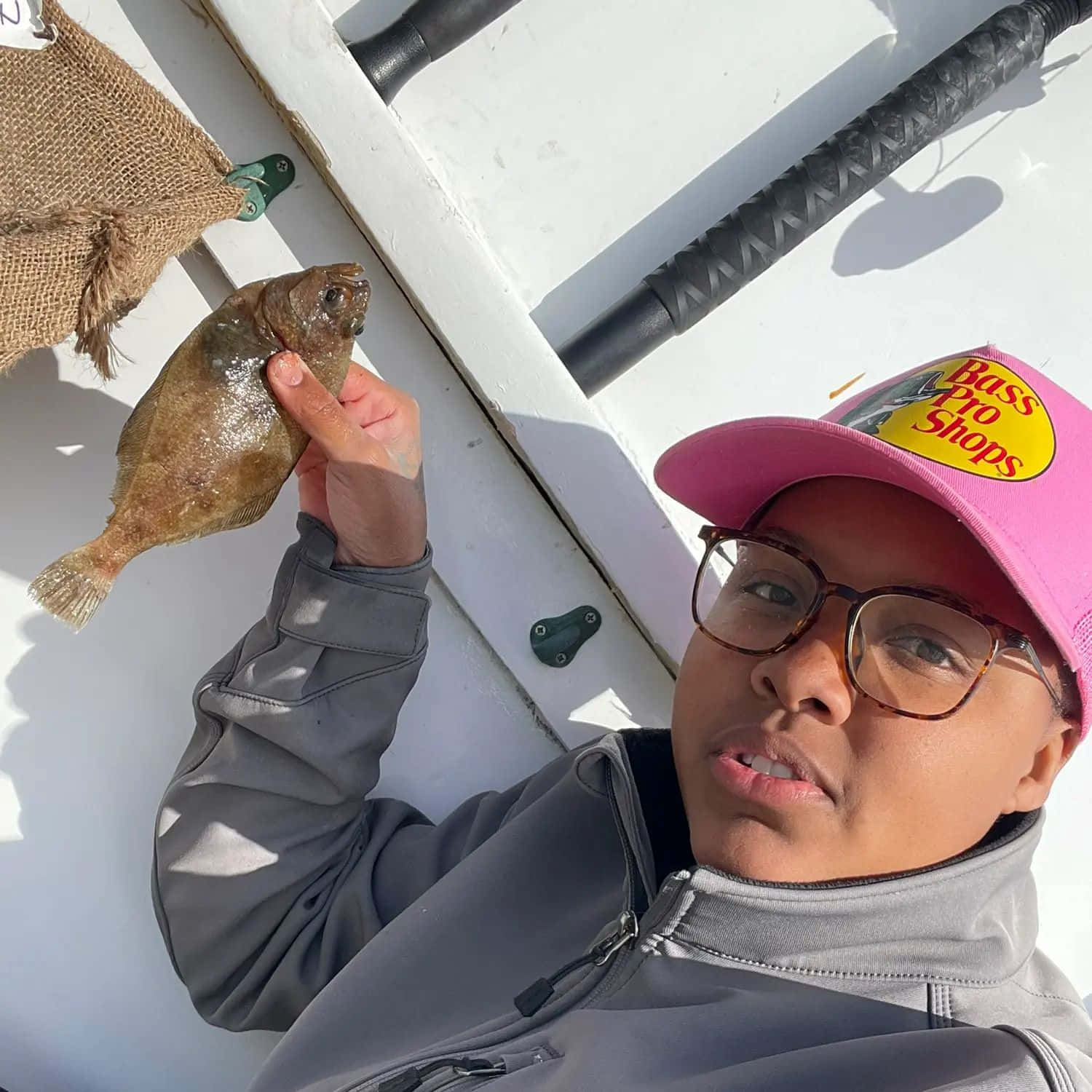  壁紙 — 一個戴粉紅色帽嘅人喺晴朗天空下嘅白色船上拎住一條啱啱捉到嘅左口魚。