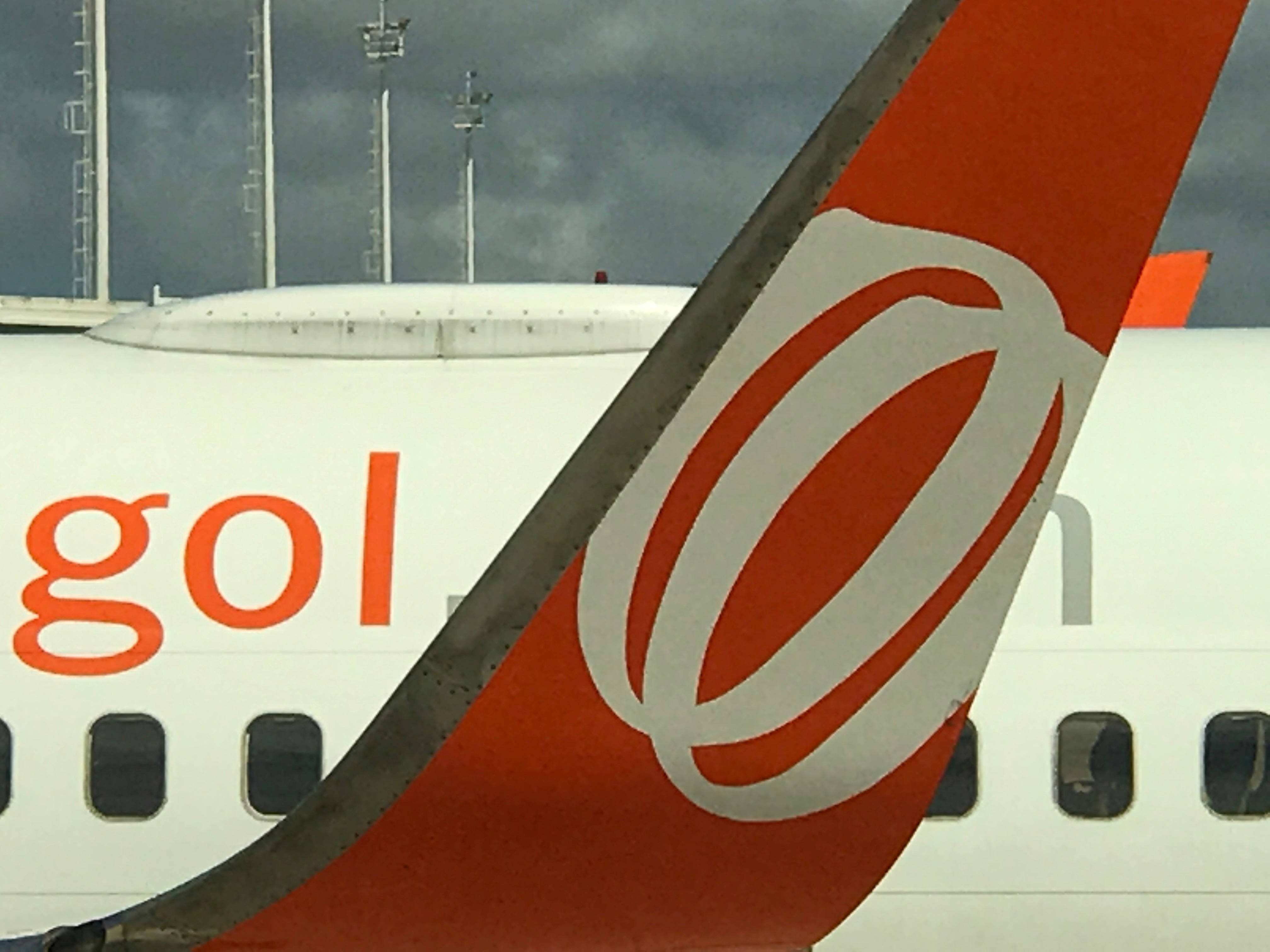 Gol 航空公司垂直尾翼標誌 壁紙 — 機場多雲天空下，戈爾航空飛機尾部特寫，帶有醒目的橙色標誌。