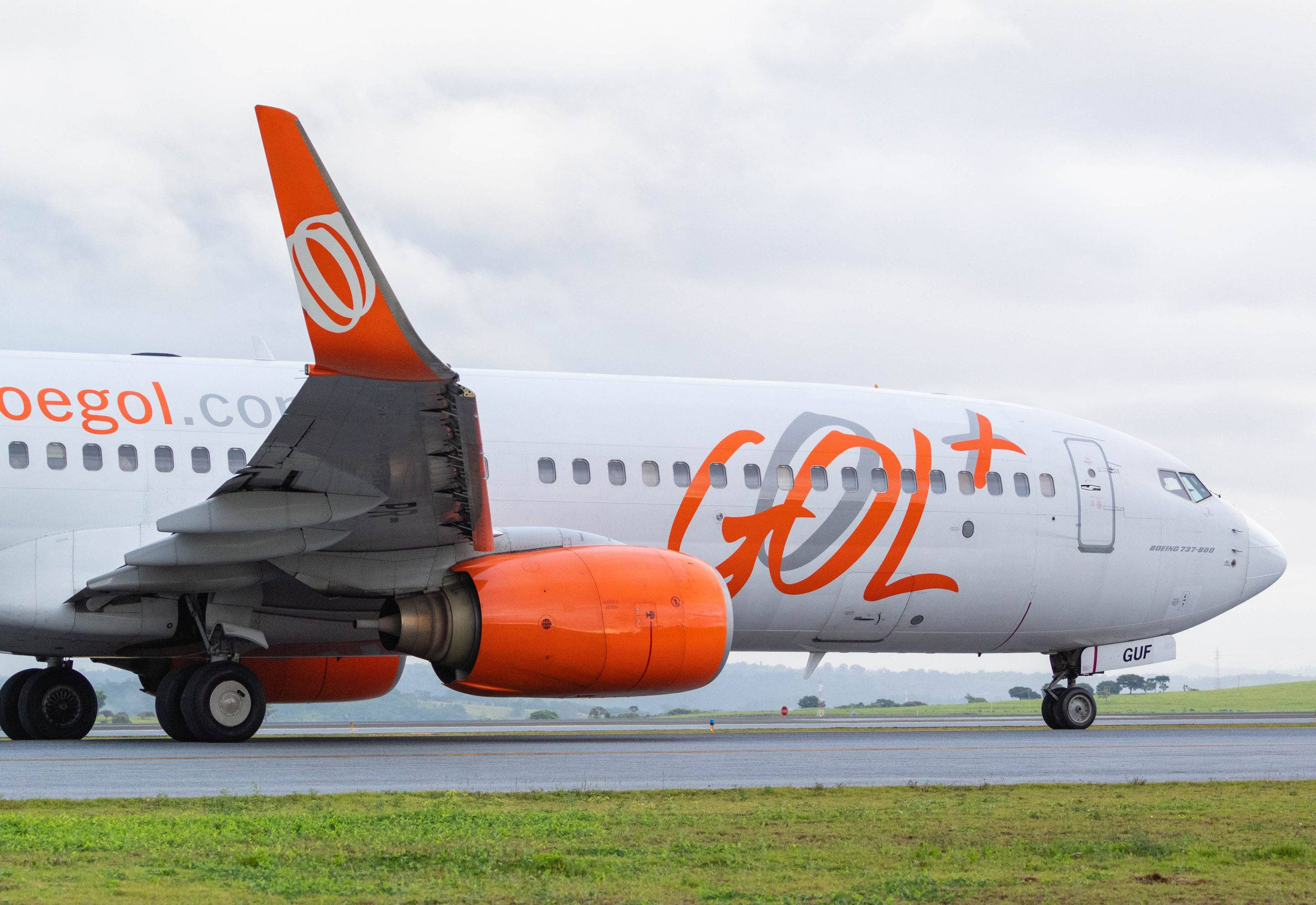 Gol 航空公司橙色引擎飛機 壁紙 — 一架帶有橙色點綴的GOL航空客機在陰天下滑行在濕滑的跑道上。