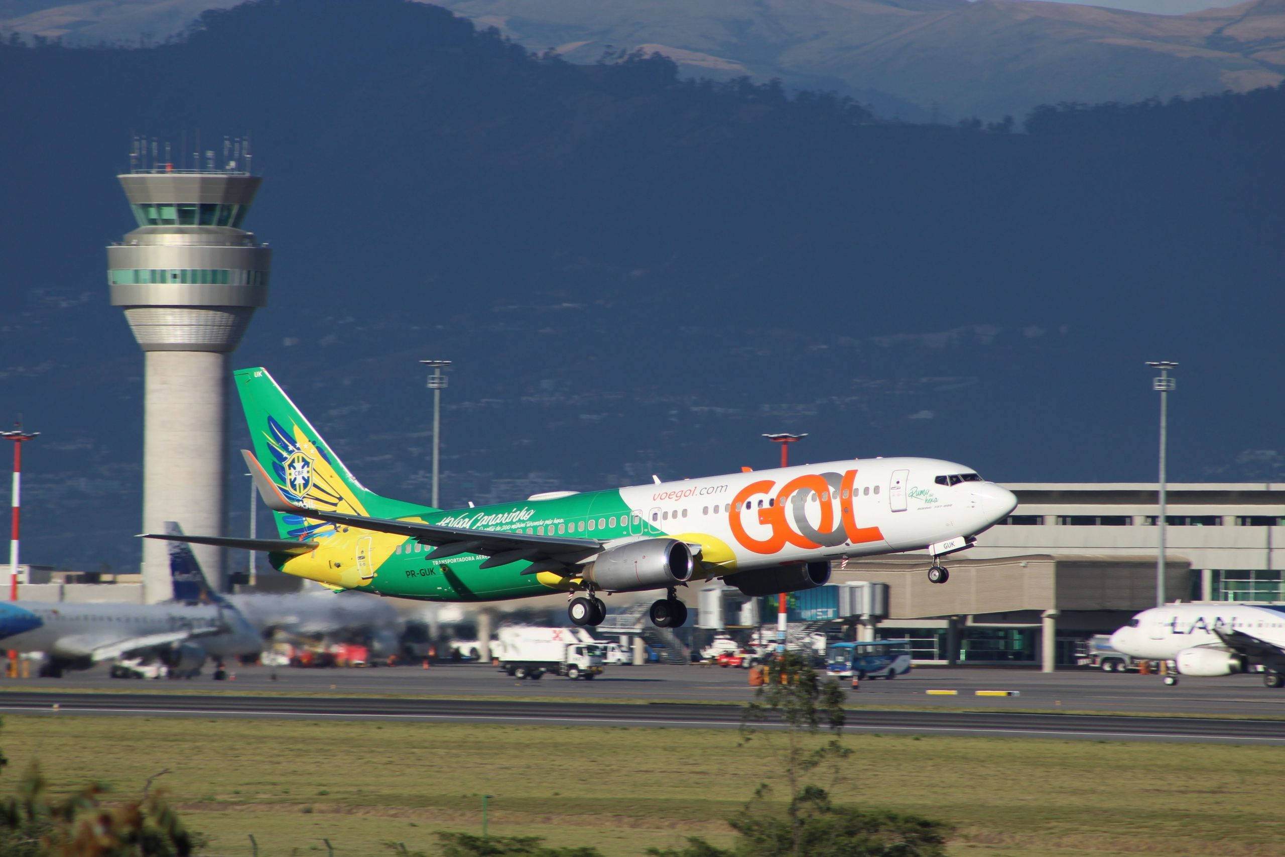 Gol 航空公司飛機起飛 壁紙 — GOL航空的飛機從機場跑道起飛，背景有控制塔和山脈。