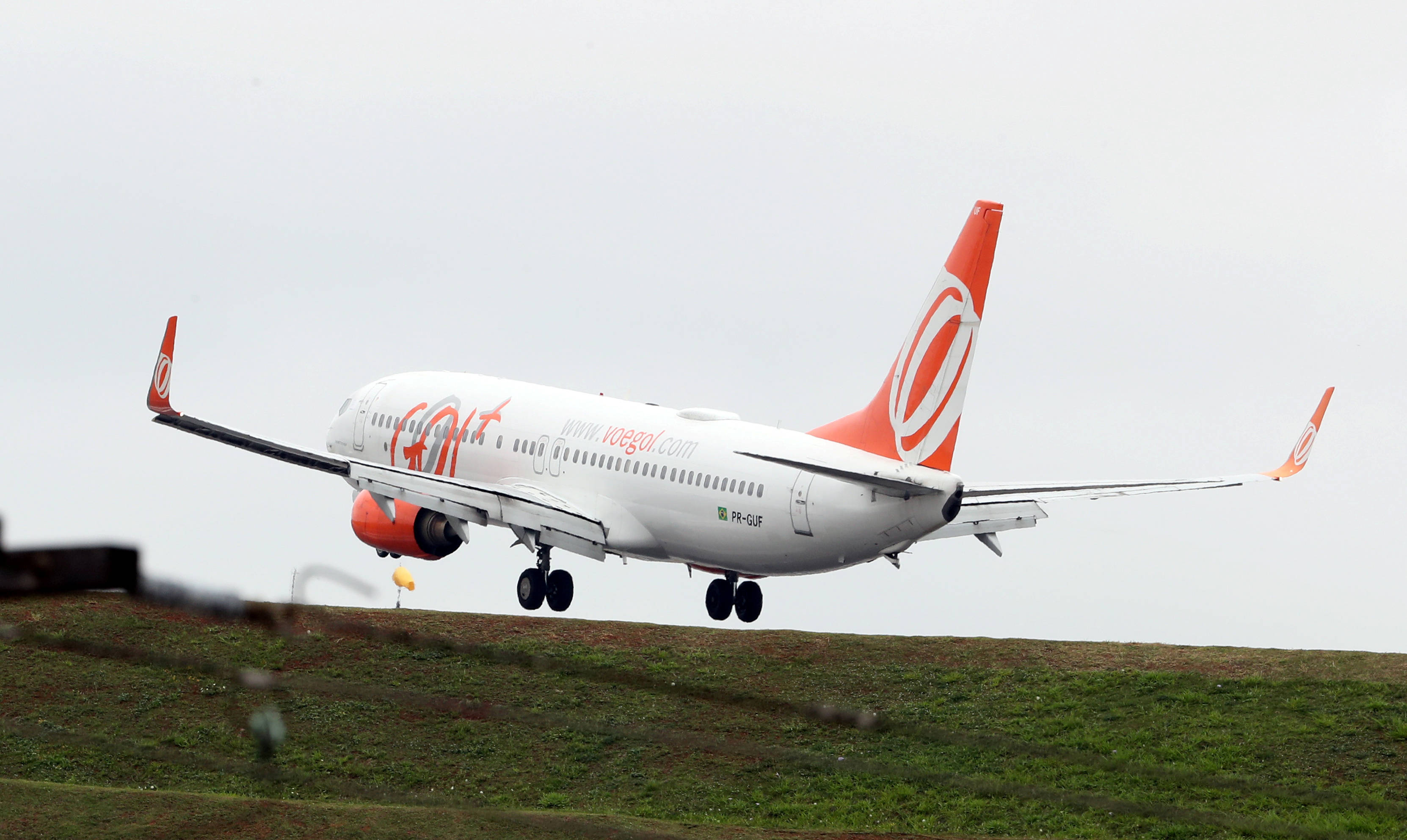Gol 航空公司飛行壯觀景象 壁紙 — 一架帶有橙色點綴的GoAir客機在灰色天空下從草地起飛。