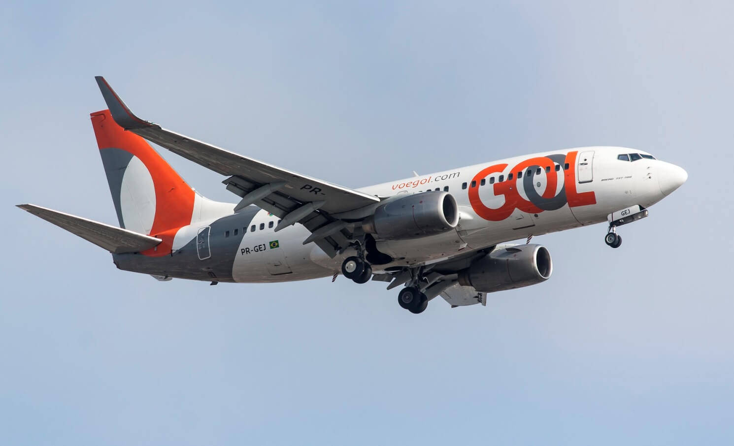 Gol 航空公司飛行於淺藍天空 壁紙 — GOL航空的波音737以橙色和白色塗裝，放下起落架，在清澈的藍天下下降。