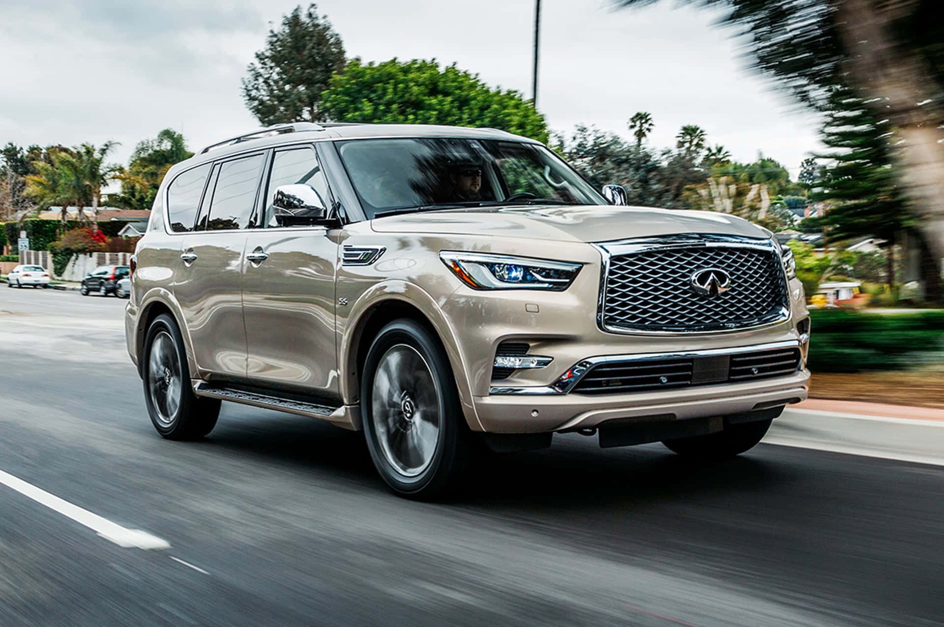 Infiniti Qx80 桌布 壁紙 — 一輛金色 Infiniti QX80 SUV 在郊區街道上飛馳，車輪和背景樹木呈現動態模糊效果。