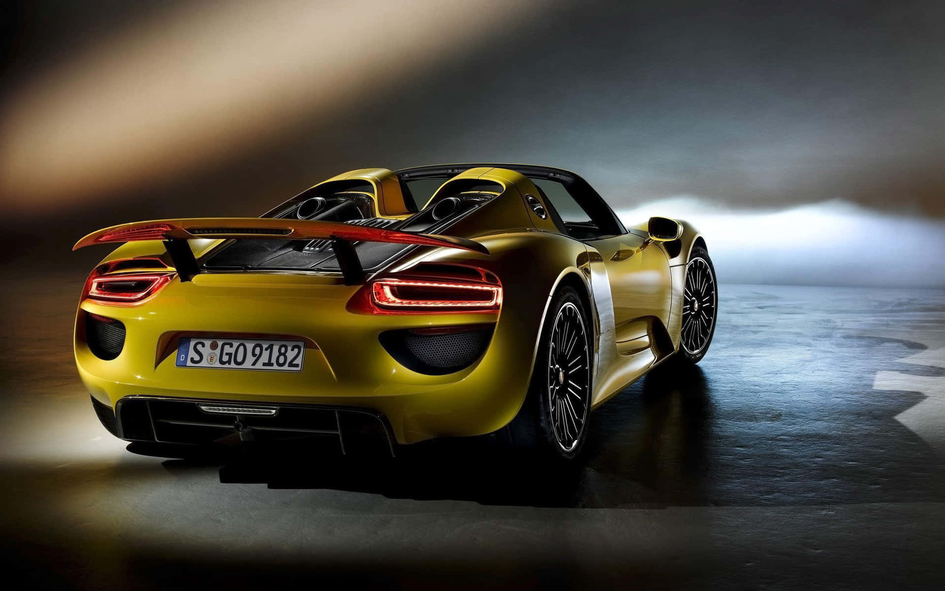 金色保時捷918 Spyder跑車在潮濕路面上，尾燈發光，在戲劇性燈光下。