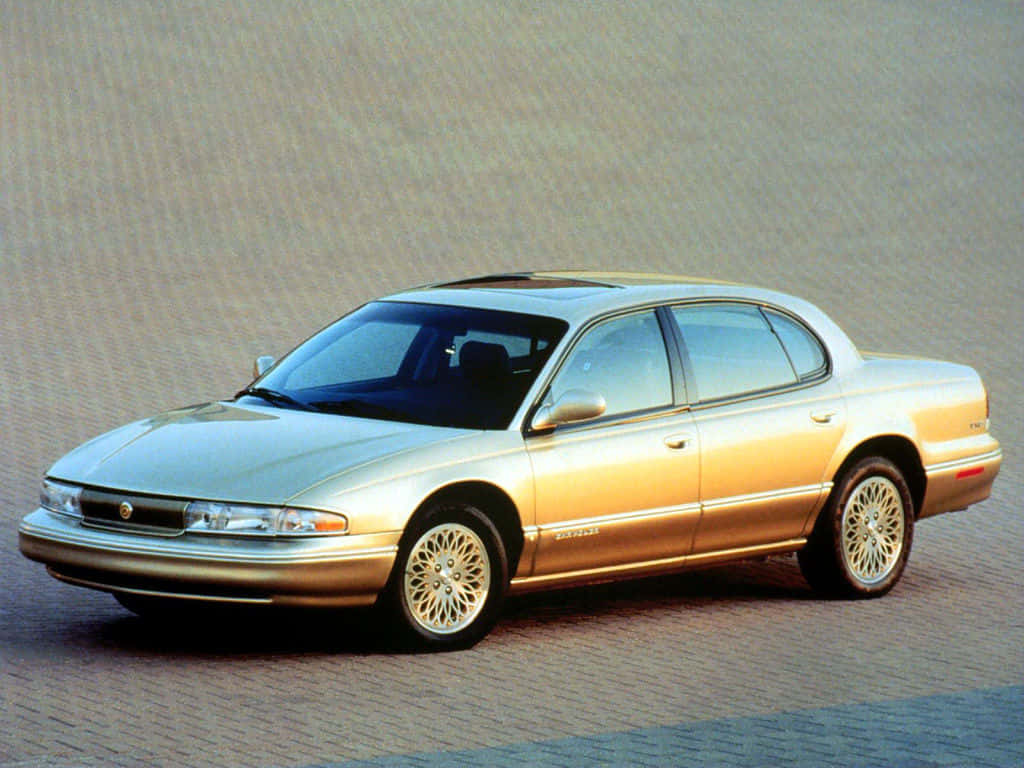 Chrysler Lhs 桌布 壁紙 — 一輛金色轎車帶有精緻的輪圈，停在鋪砌路面上，處於明亮日光下。