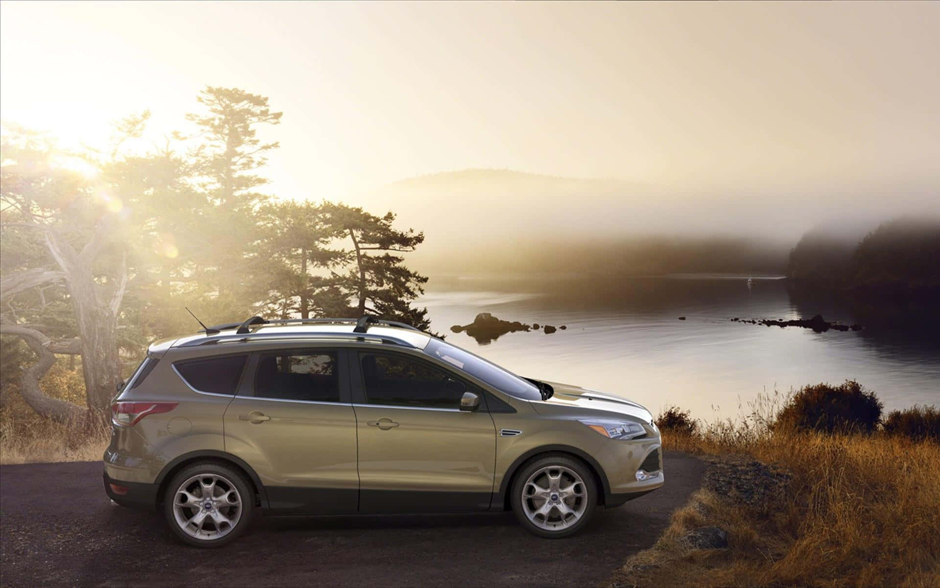 Ford Escape 桌布 壁紙 — 一輛金色SUV停泊在霧氣瀰漫的湖邊道路上，日出時分，樹木和遠山在金色光芒中閃耀。