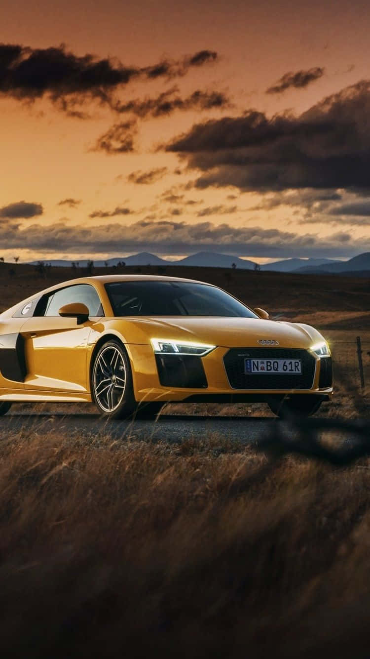 Sunset Drive 桌布 壁紙 — 一輛金色奧迪R8跑車在戲劇性的日落天空下閃閃發光，天空有烏雲和遠山。