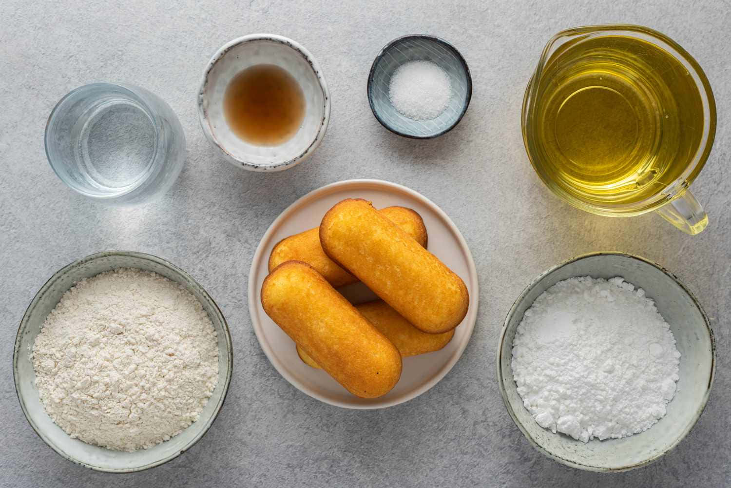  壁紙 — 金黃色的玉米熱狗放在碟上，周圍有碗裝的麵粉、糖、水和油，置於灰色檯面上。