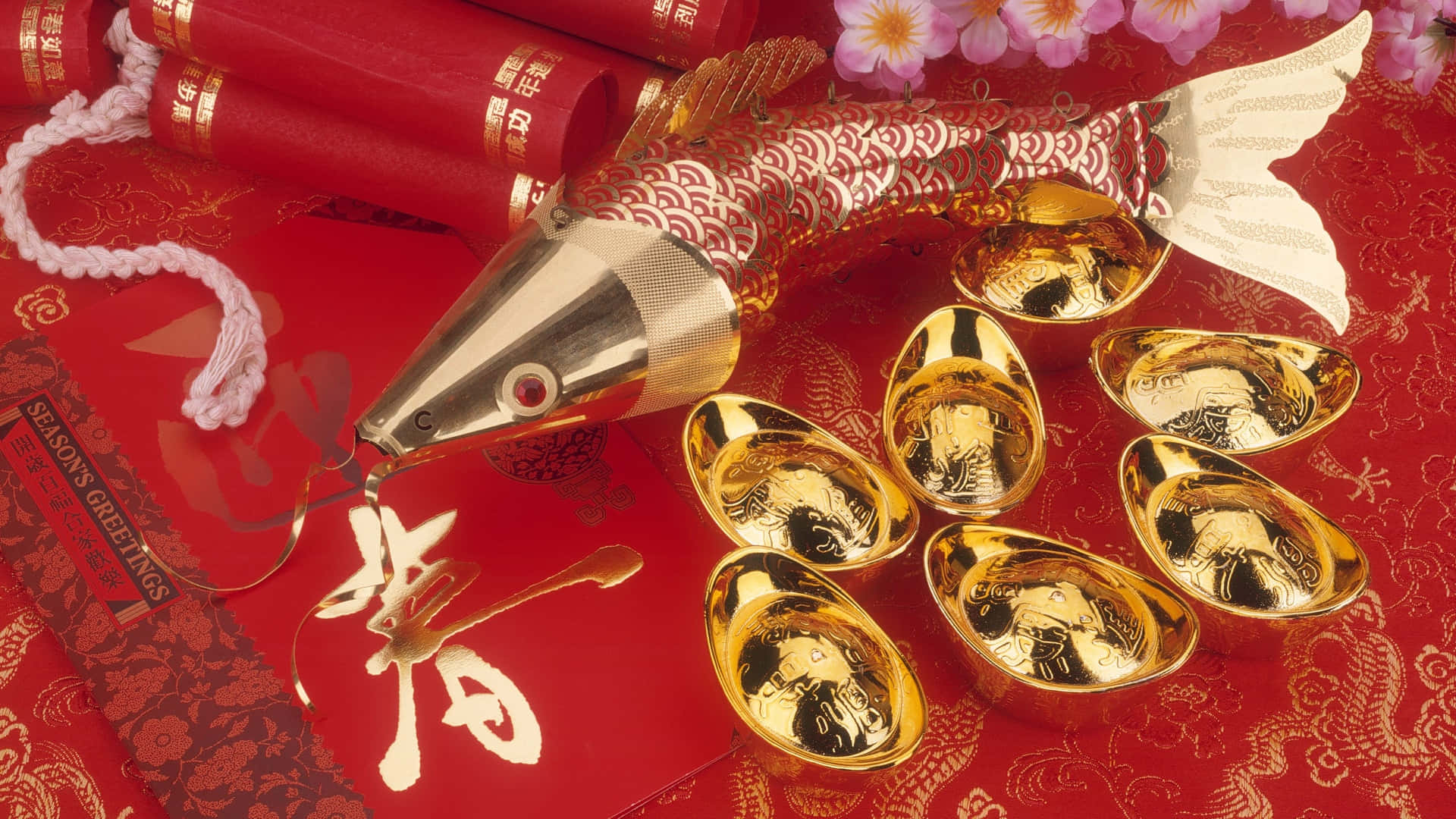  壁紙 — 金色魚形裝飾和元寶放在帶有花卉圖案和中文文字的紅紙上，營造節日慶祝氣氛。
