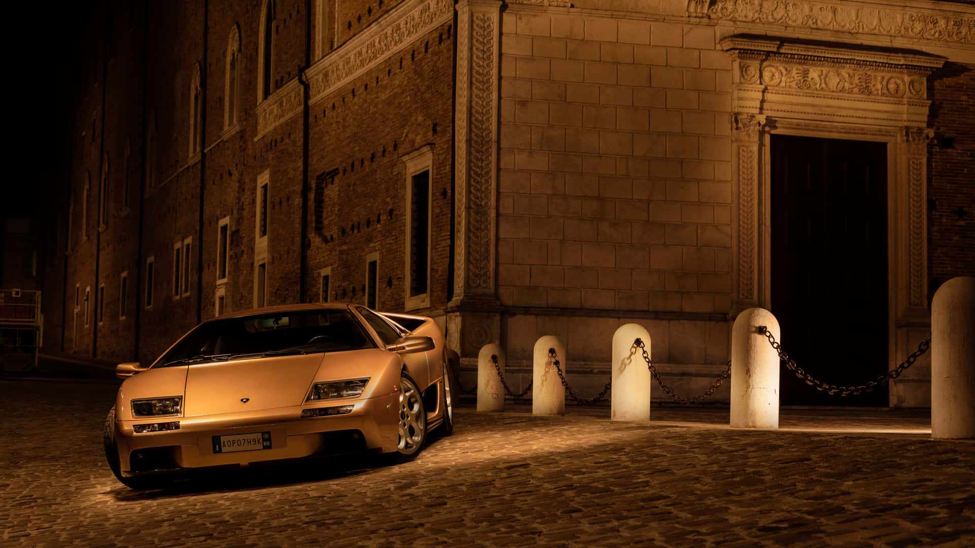 Lamborghini Diablo 桌布 壁紙 — 一輛金色林寶堅尼Diablo在夜晚停泊在鵝卵石街道上，旁邊是一座華麗的石建築。