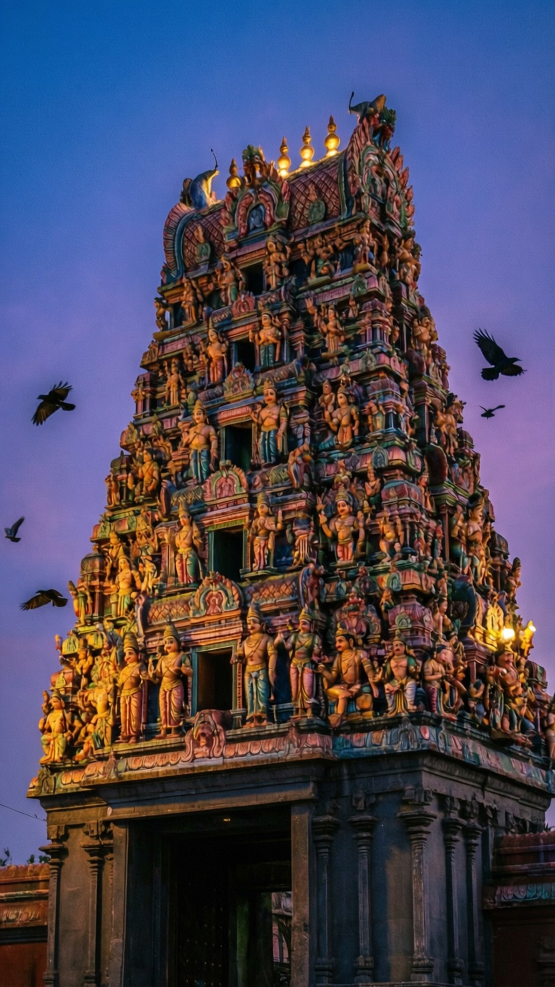 Chennai 桌布 壁紙 — 一座高聳、雕刻精美的印度教寺廟 gopuram，沐浴在金色暮光中，鳥兒在紫色天空下飛翔。