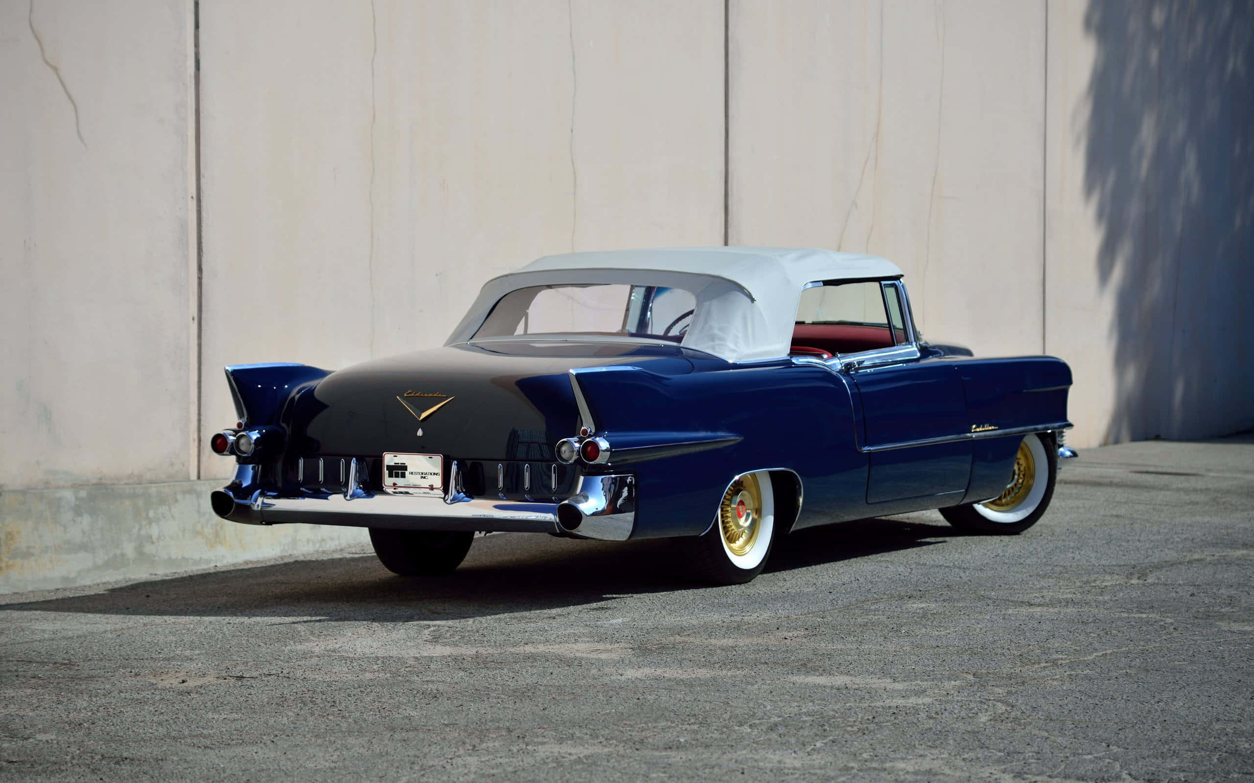 Cadillac Eldorado 桌布 壁紙 — 一架光面藍色經典開篷車，白色軟頂，停泊在瀝青地面上的素牆旁。