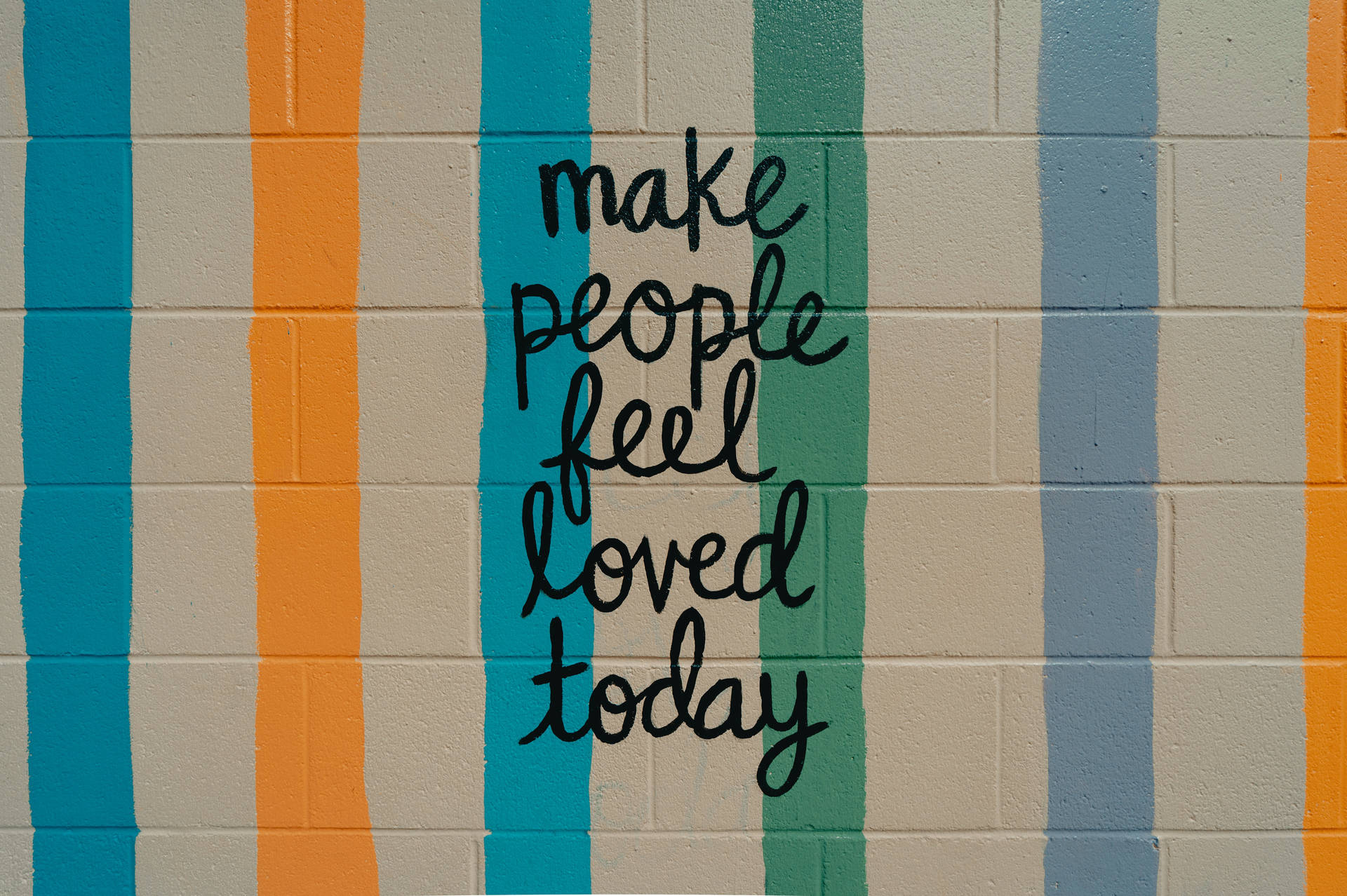 彩色條紋牆上寫有手寫訊息「make people feel loved today」