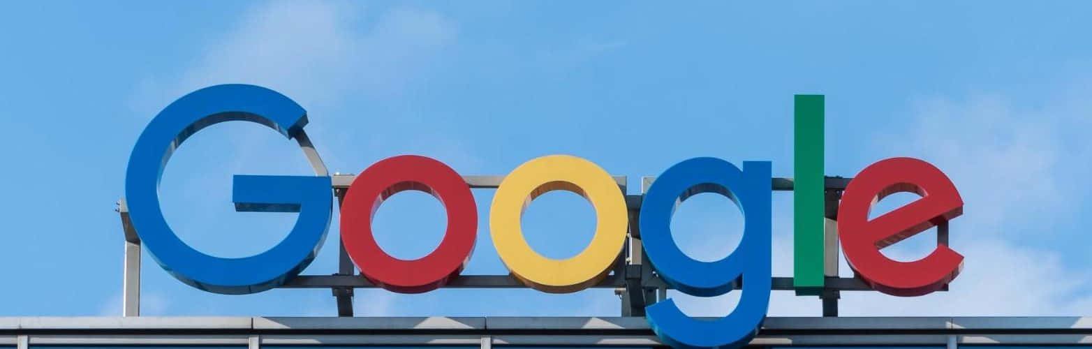 Google Drive 公司標誌 壁紙 — Google 標誌性的多色標誌在晴朗藍天和薄雲襯托下顯得格外醒目。